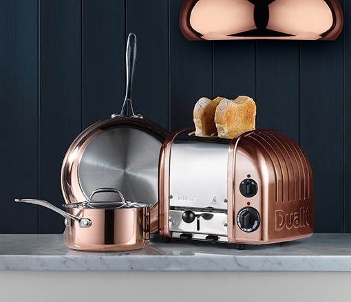Kupfer-Toaster mit Brot und Kupferpfannen auf Marmorarbeitsplatte.