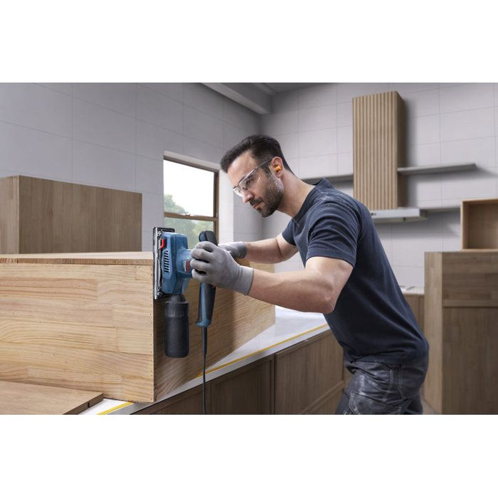 Mann schleift Holzmöbel mit blauem Schleifgerät, trägt Schutzbrille und Handschuhe.