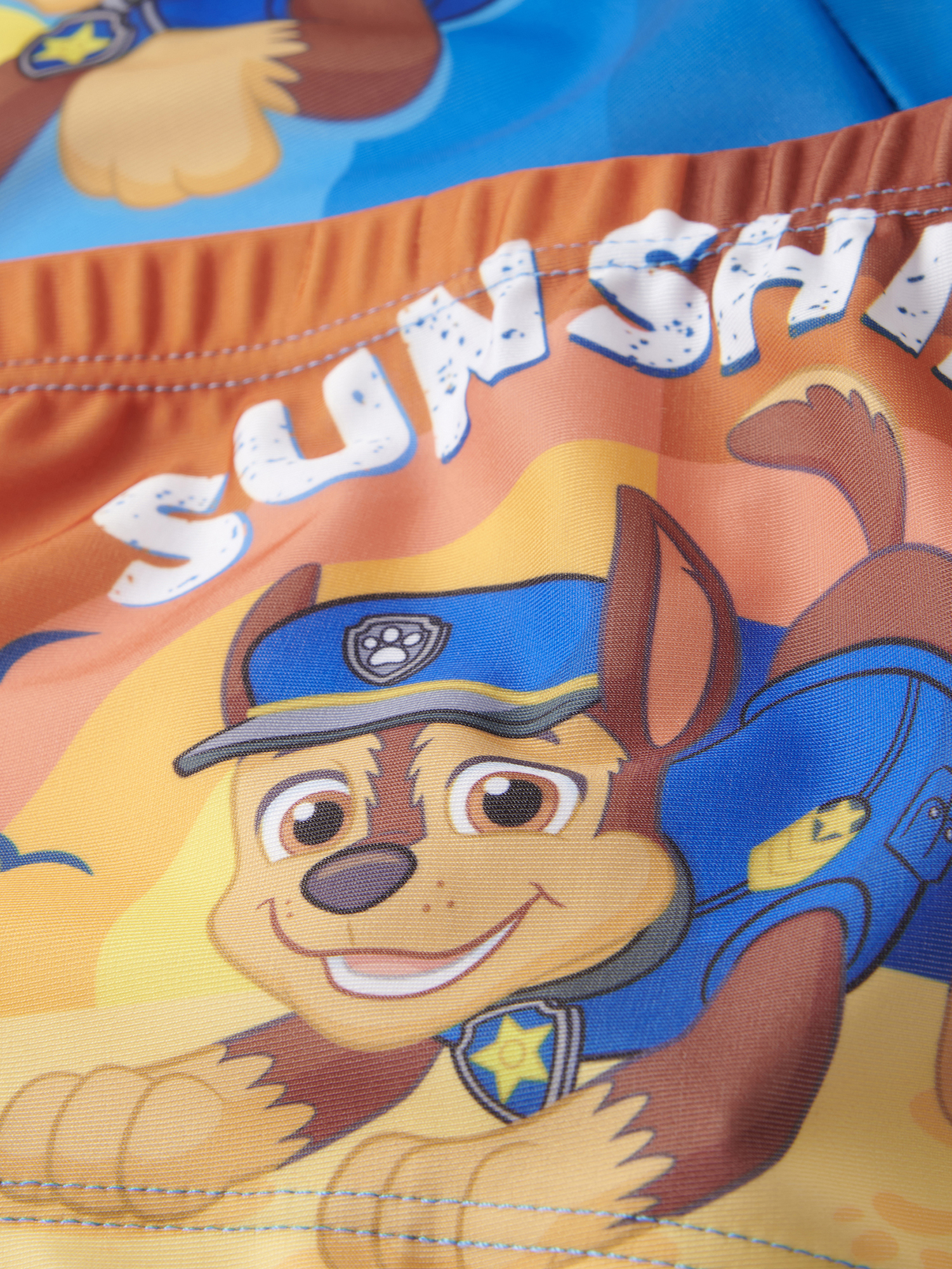 Chase von Paw Patrol trägt eine blaue Uniform und einen blauen Hut. Der Hintergrund ist orange und gelb.