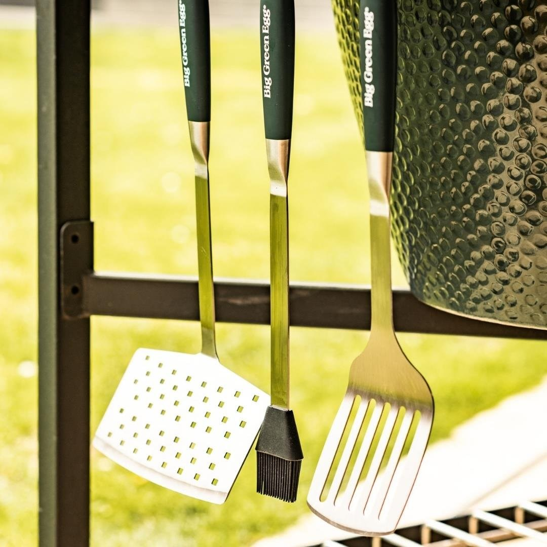 Yeşil saplı üç Big Green Egg ızgara aleti bir rafta asılı duruyor.