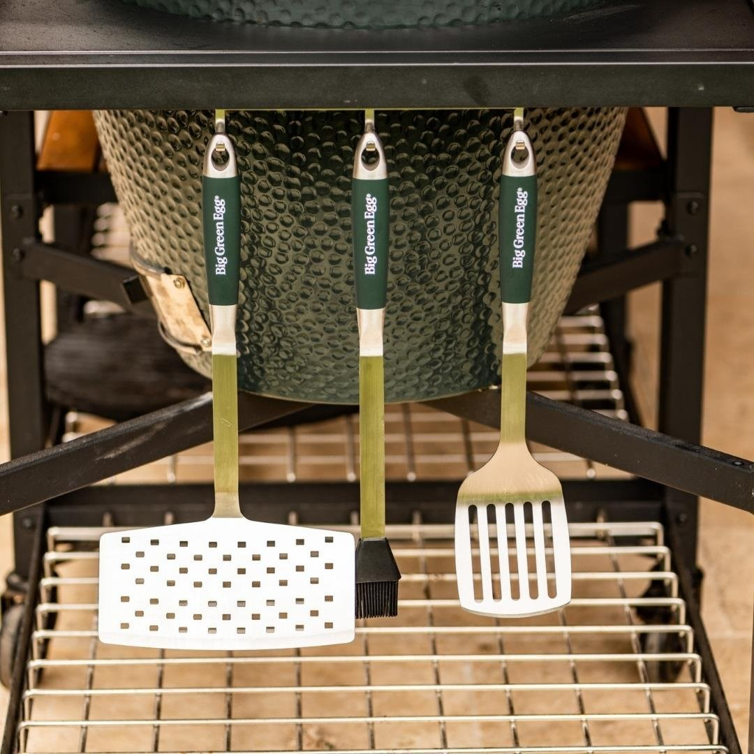 Yeşil saplı barbekü aletleri, Big Green Egg ızgarasına asılı duruyor.