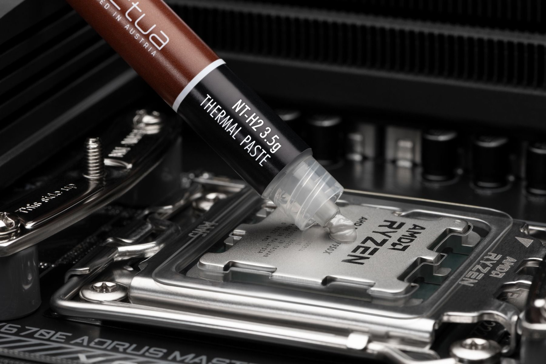 Eine braune Tube mit NT-H2 3,5g Wärmeleitpaste wird auf eine AMD Ryzen CPU aufgetragen.