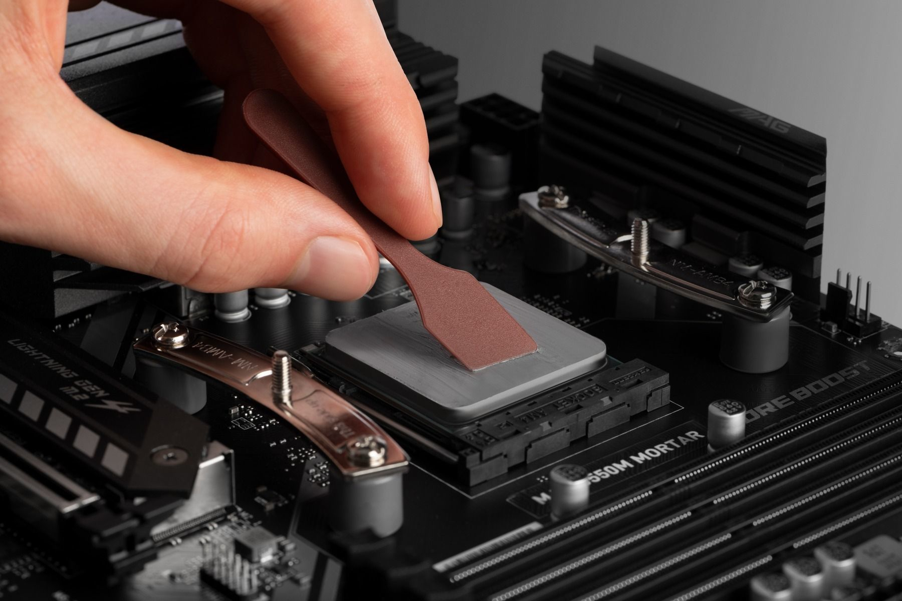 Ein Finger verteilt Wärmeleitpaste auf einem Computerprozessor auf einem Motherboard.