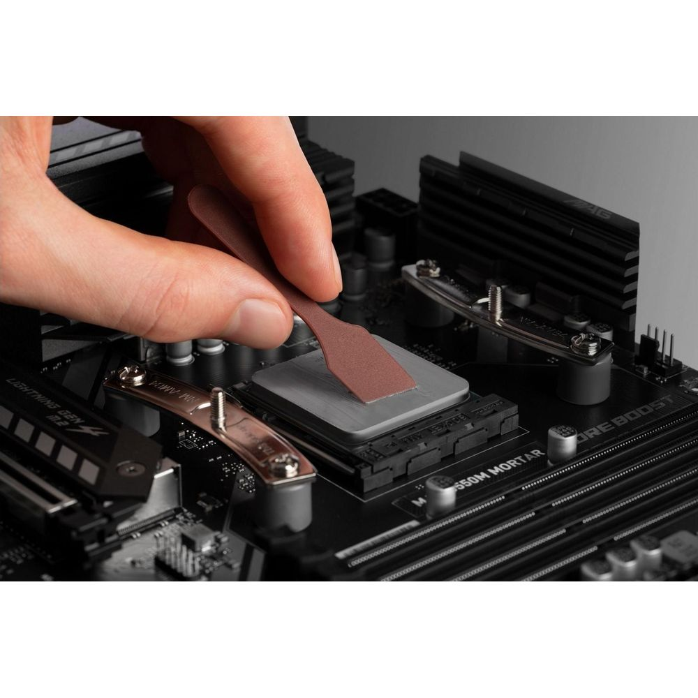 Eine Hand verteilt Wärmeleitpaste auf einer Computer-CPU mit einem Spatel auf einem Motherboard.