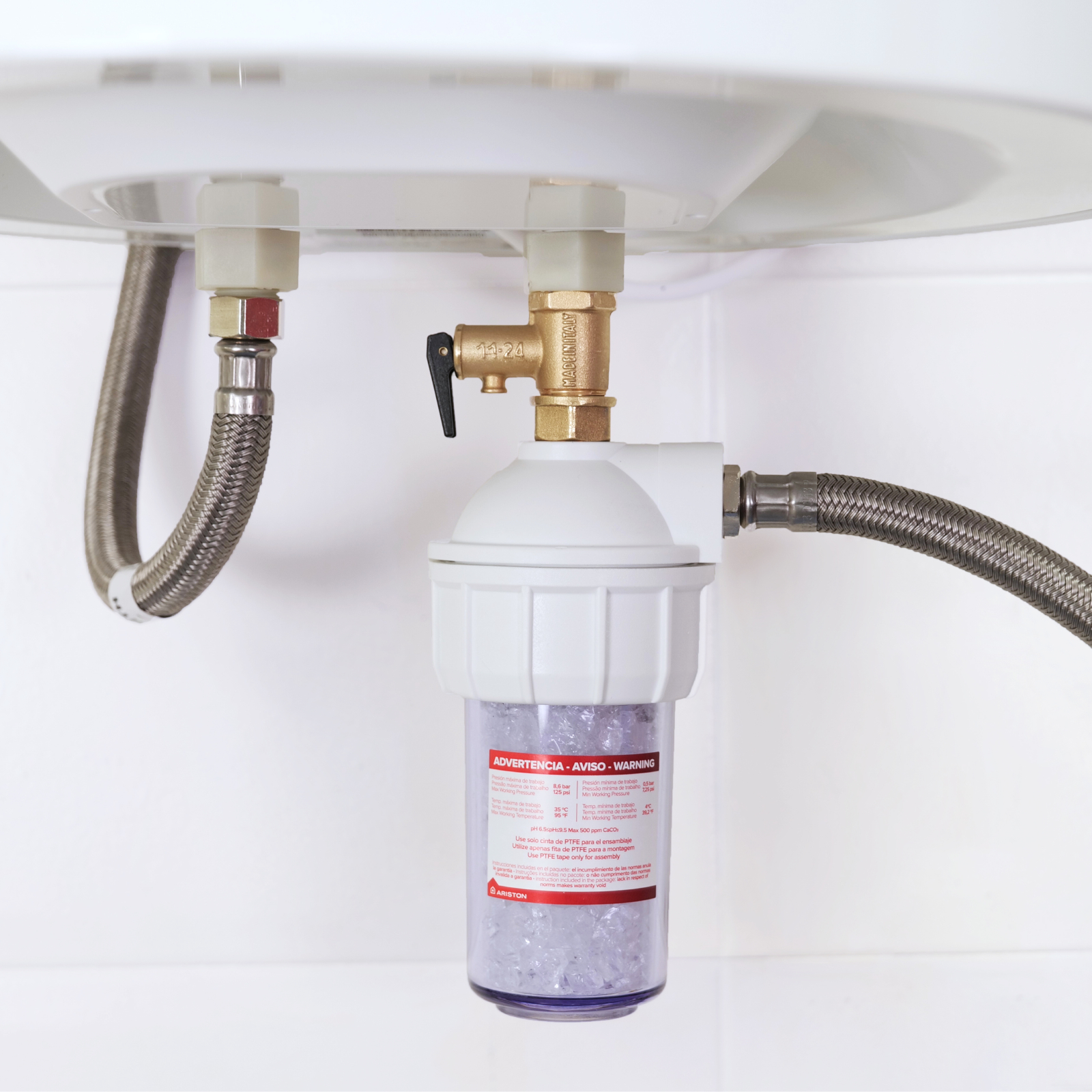 Un filtro de agua con válvula de latón y mangueras flexibles unido a un aparato blanco.