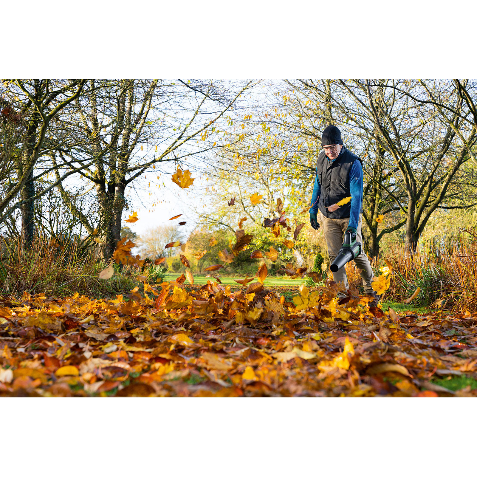 Mann bläst mit Laubbläser Blätter im Herbstpark.