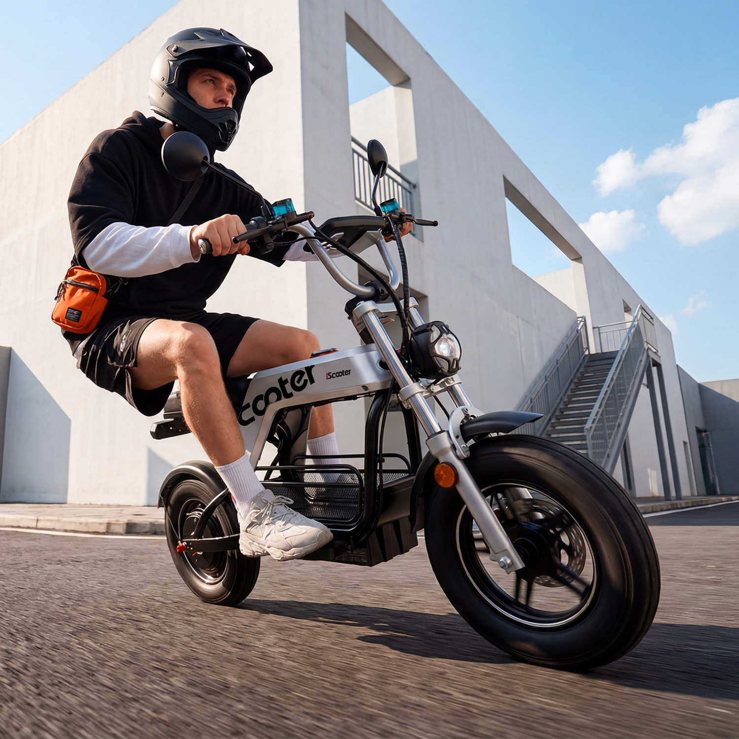 Hombre con casco montando una bicicleta eléctrica plateada en una carretera frente a un edificio moderno.