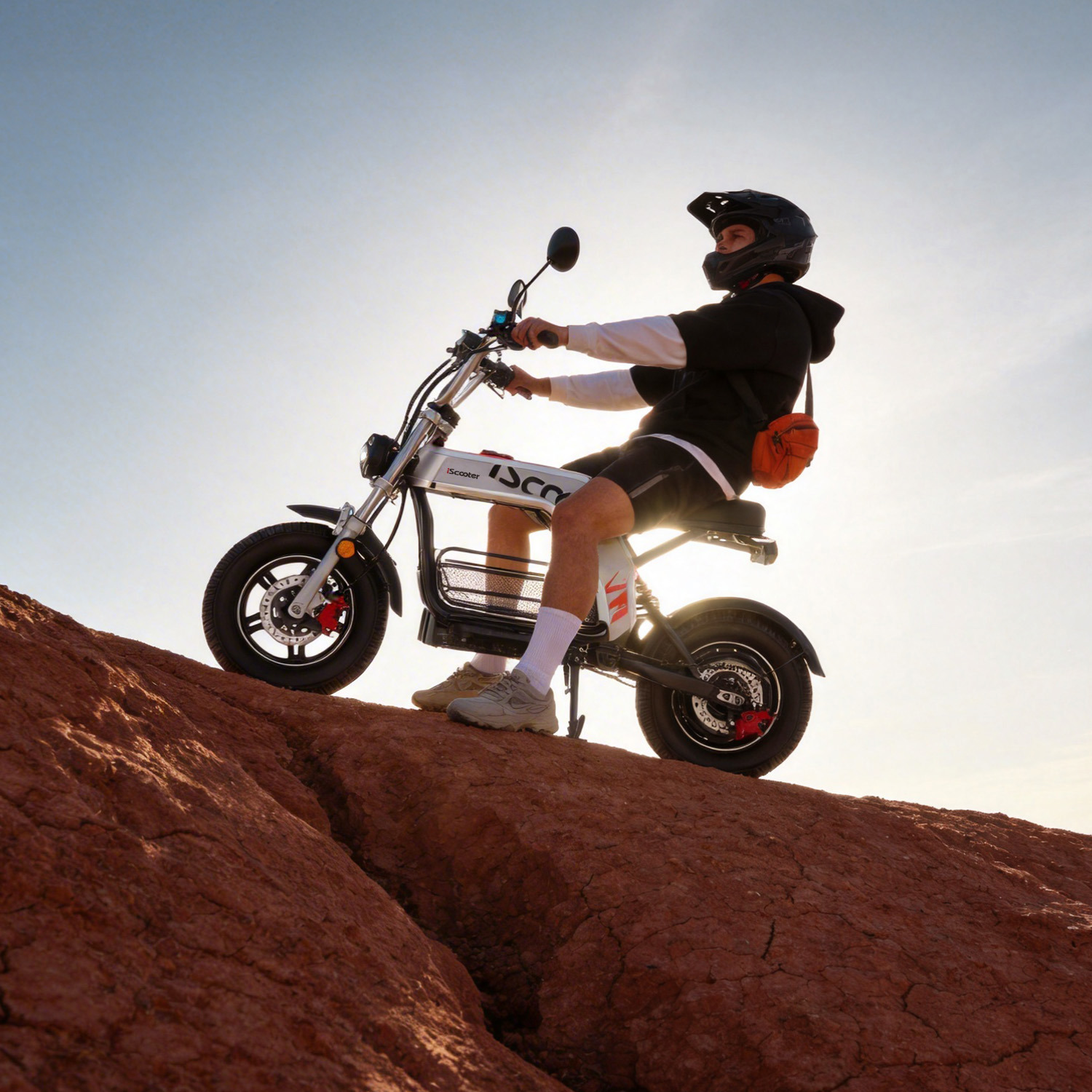 Hombre con casco monta scooter eléctrico en colina rocosa cielo brillante.