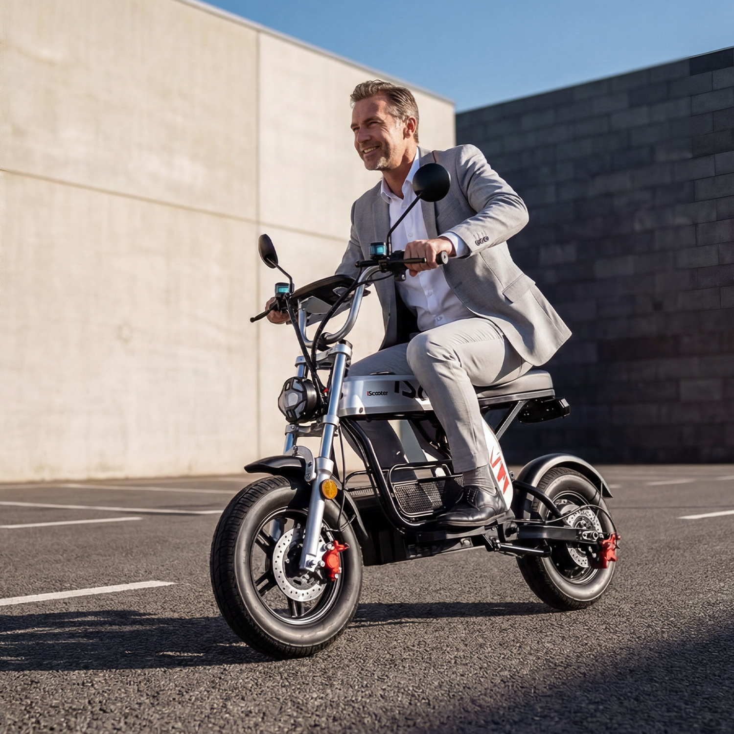 Un hombre sonriente con traje gris monta una scooter eléctrica blanca y negra en una carretera pavimentada.