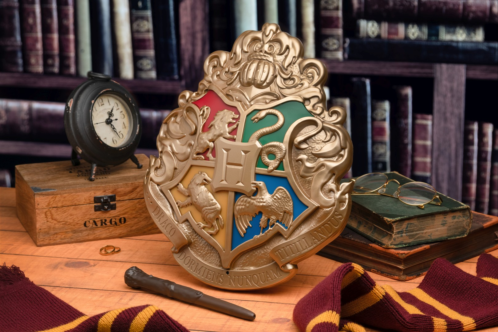 Herb Hogwartu, różdżka, szalik, zegar, książki i pierścienie na drewnianym stole.