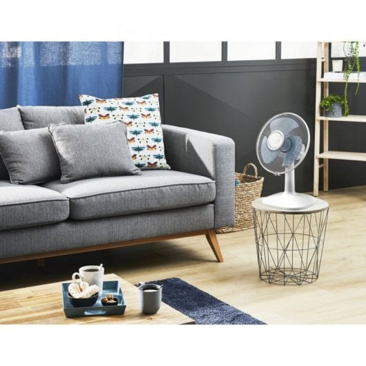 Un sofá gris con cojines y un ventilador en una mesita auxiliar.