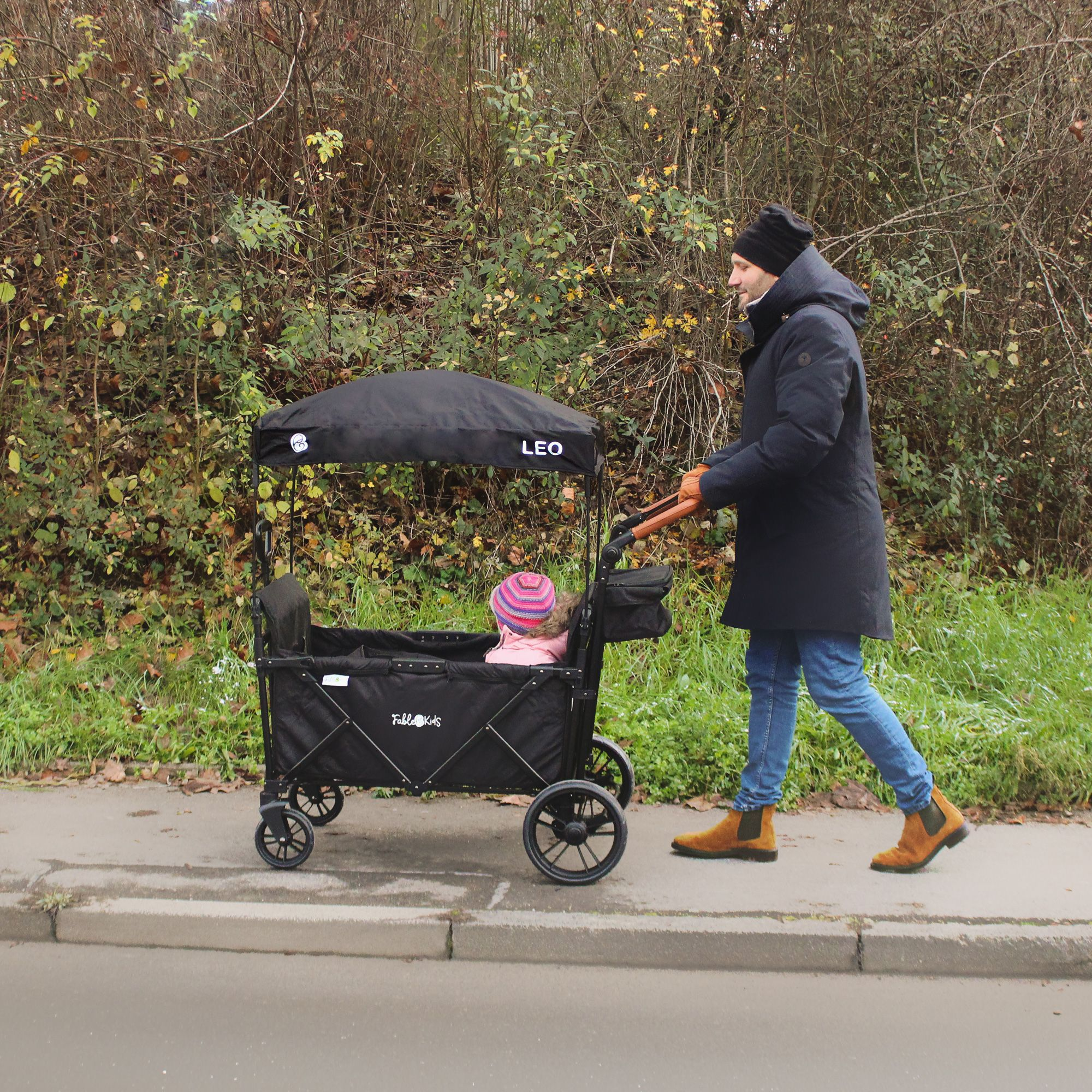 Ein Mann schiebt einen Kinderwagen mit einem Baby auf einem Gehweg neben Bäumen.