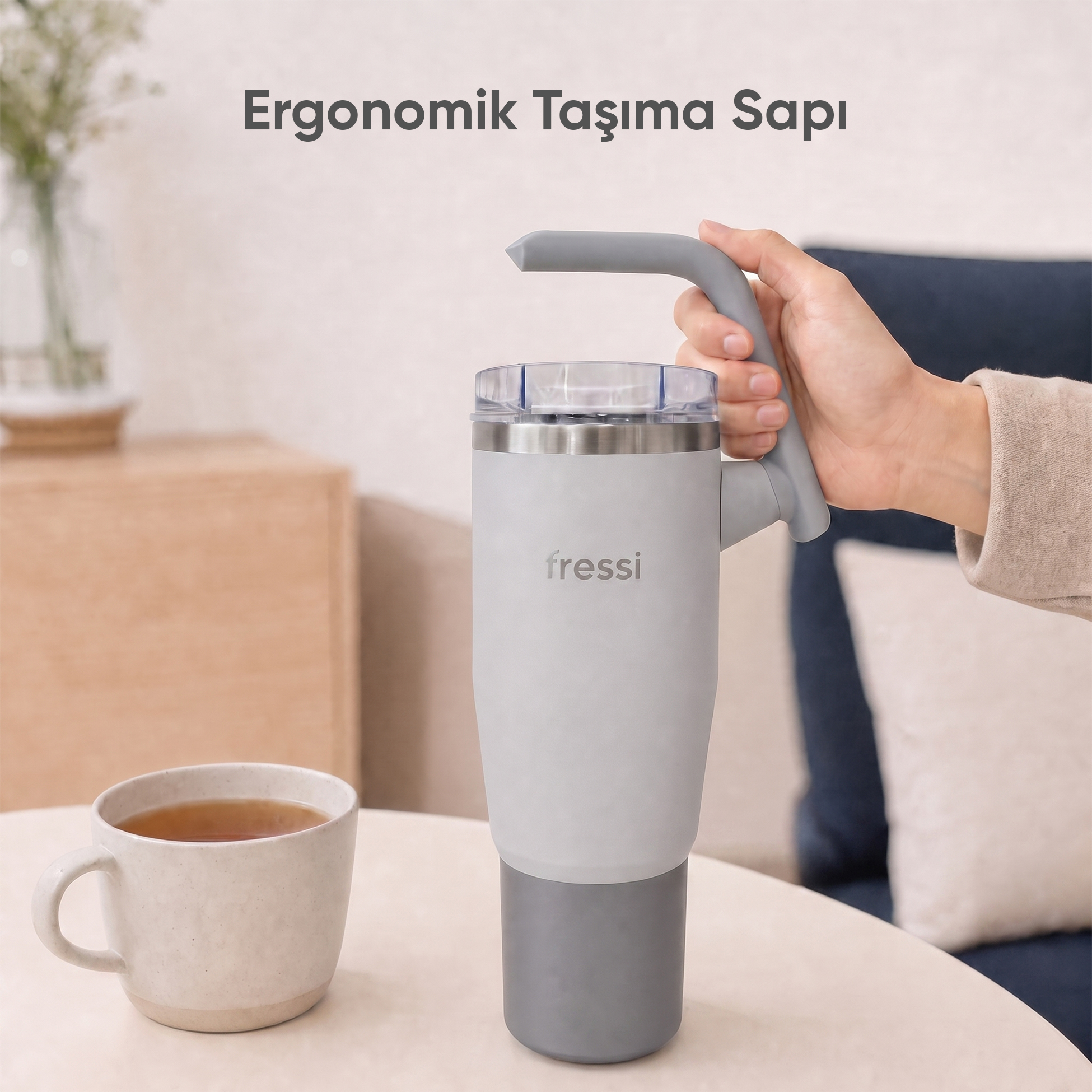 Bir el, kulplu gri termos bardak tutuyor. Yanında bir fincan çay var.