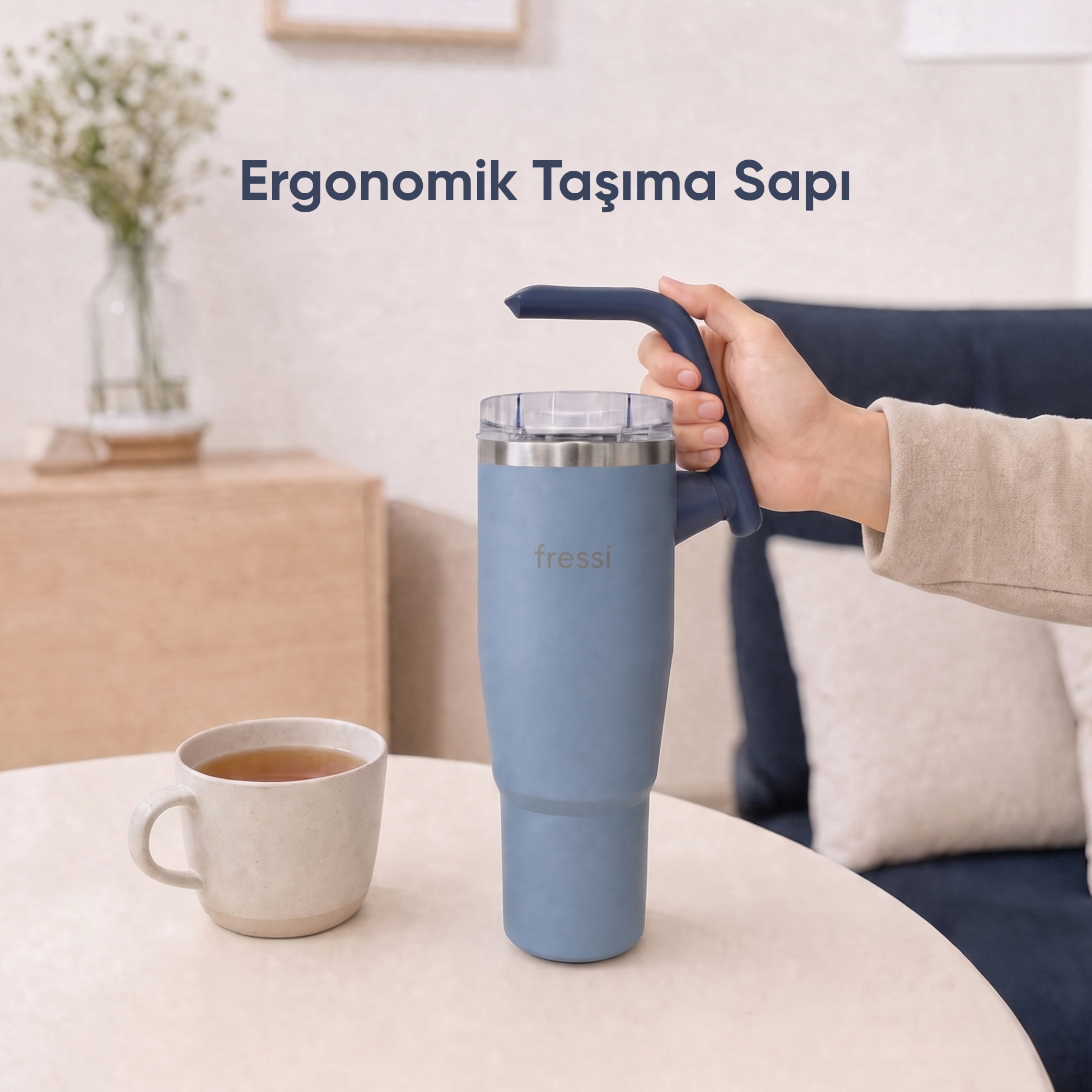 Bir el, saplı mavi bir kupa tutuyor. Yanında bir fincan çay var.
