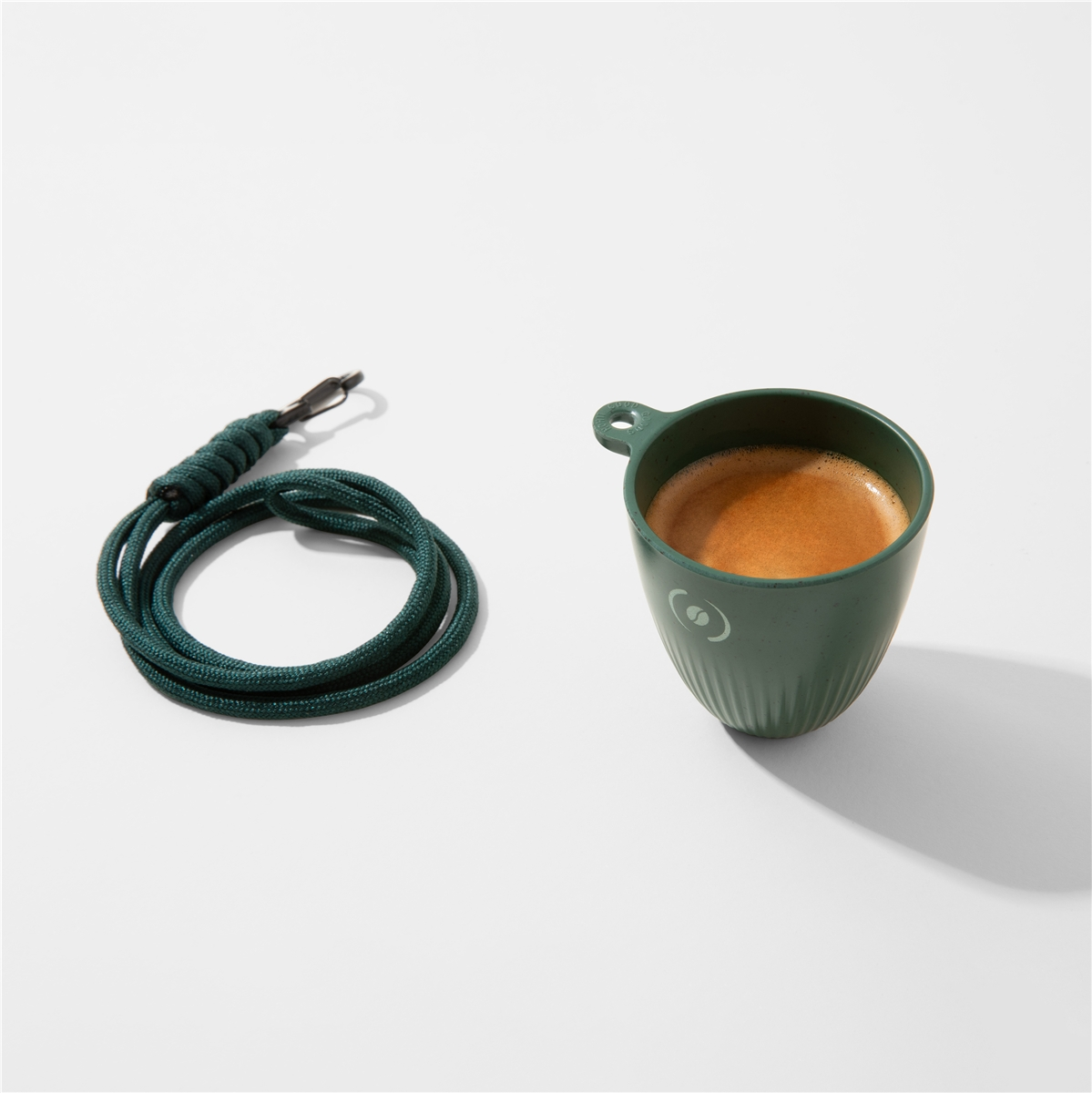 Una tazza verde di espresso con crema accanto a un cordone verde scuro arrotolato con clip metallica.