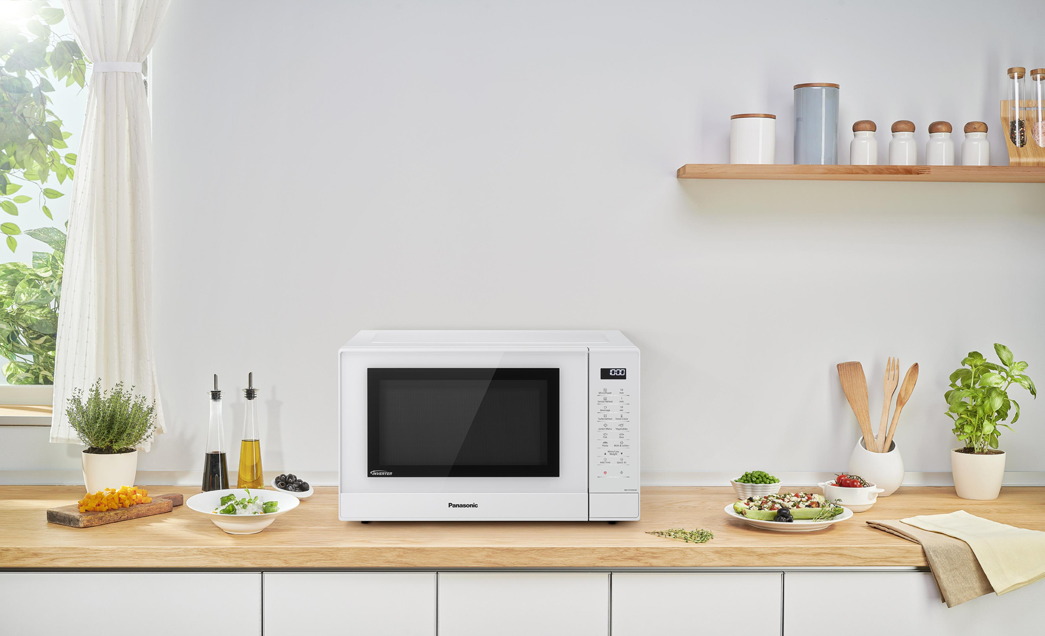 Un microondas blanco sobre una encimera de madera con comida y utensilios.