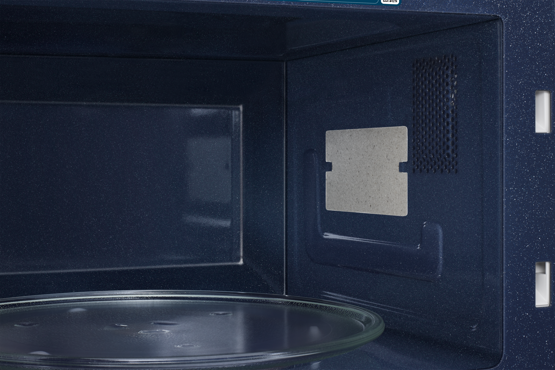 Interno microonde scuro con piatto girevole in vetro e griglia ventilazione.