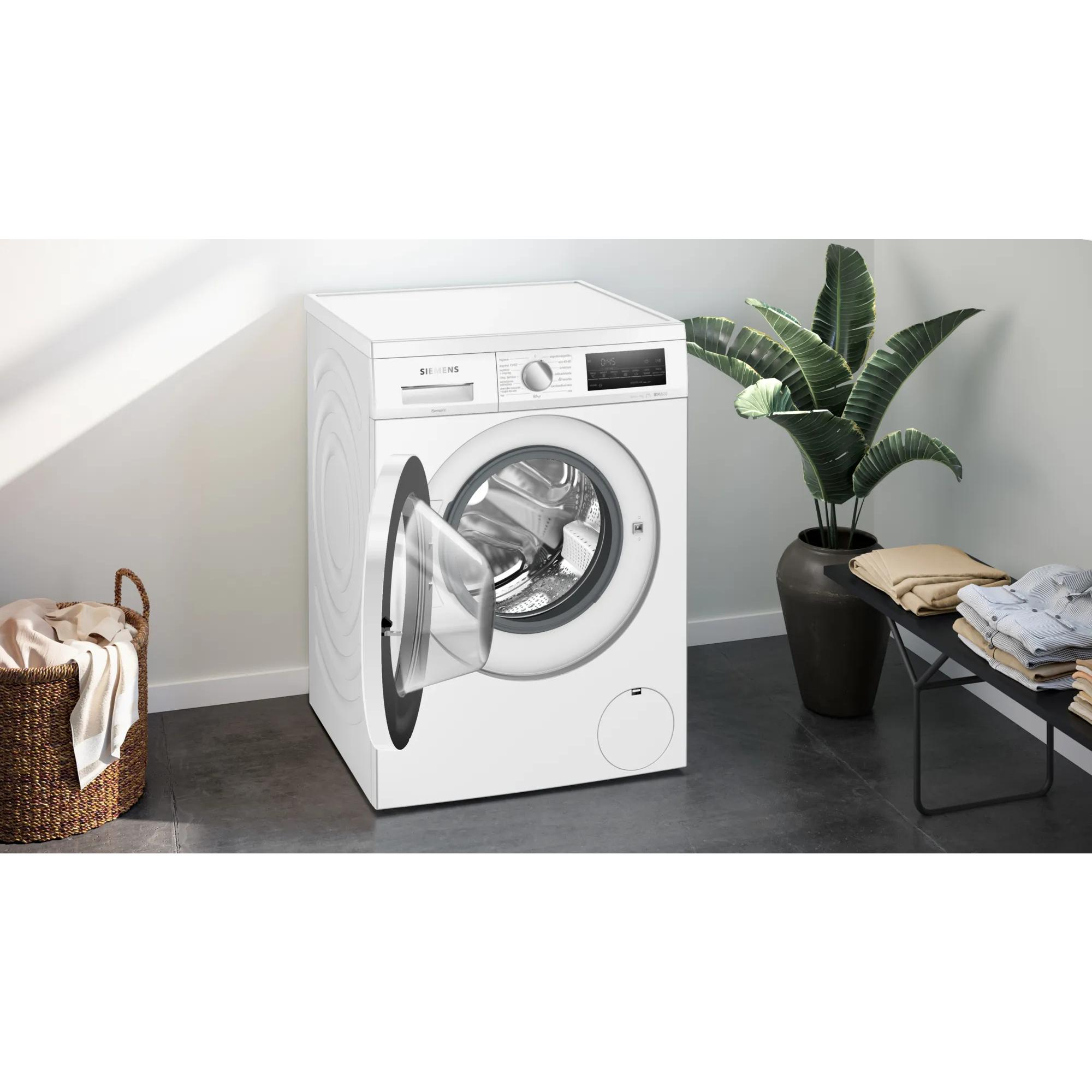 Una lavatrice Siemens bianca con porta aperta accanto a un cesto per la biancheria.
