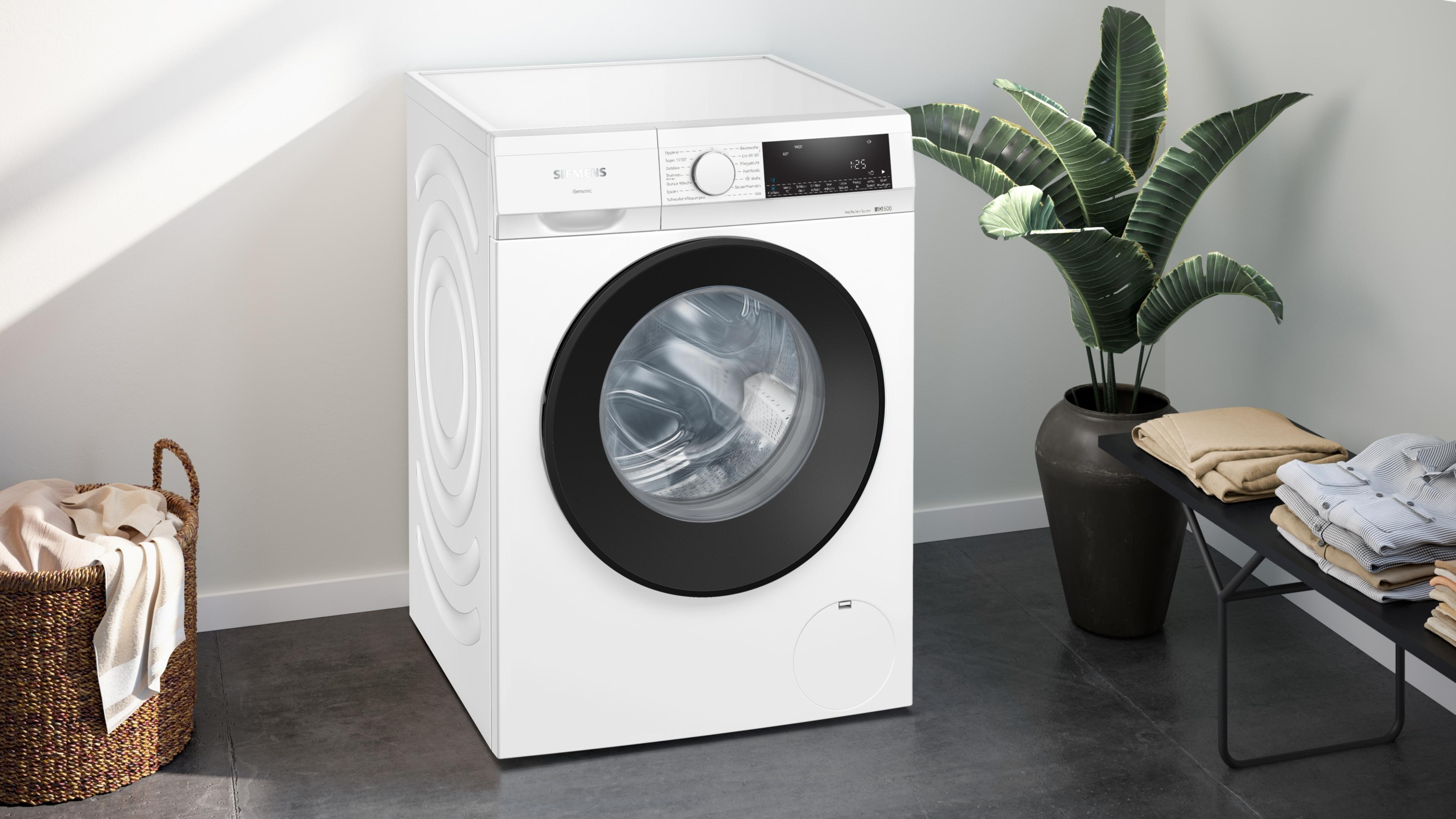 Eine weiße Siemens Waschmaschine steht neben einem Wäschekorb und einer Pflanze.