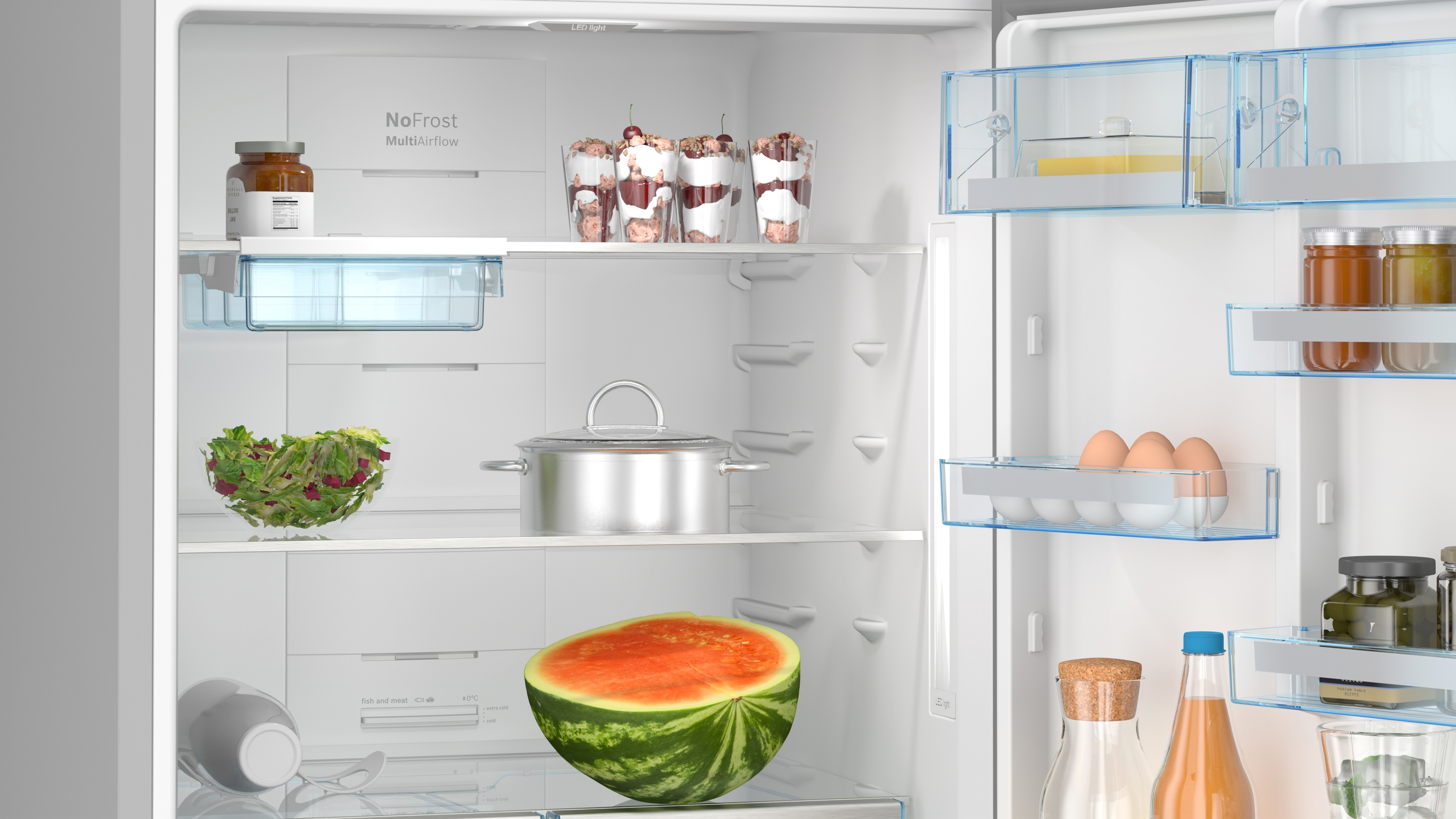 Offener Kühlschrank mit Lebensmitteln: Wassermelone, Salat, Gläser mit Dessert, Topf, Eier, Flaschen und Gläser.
