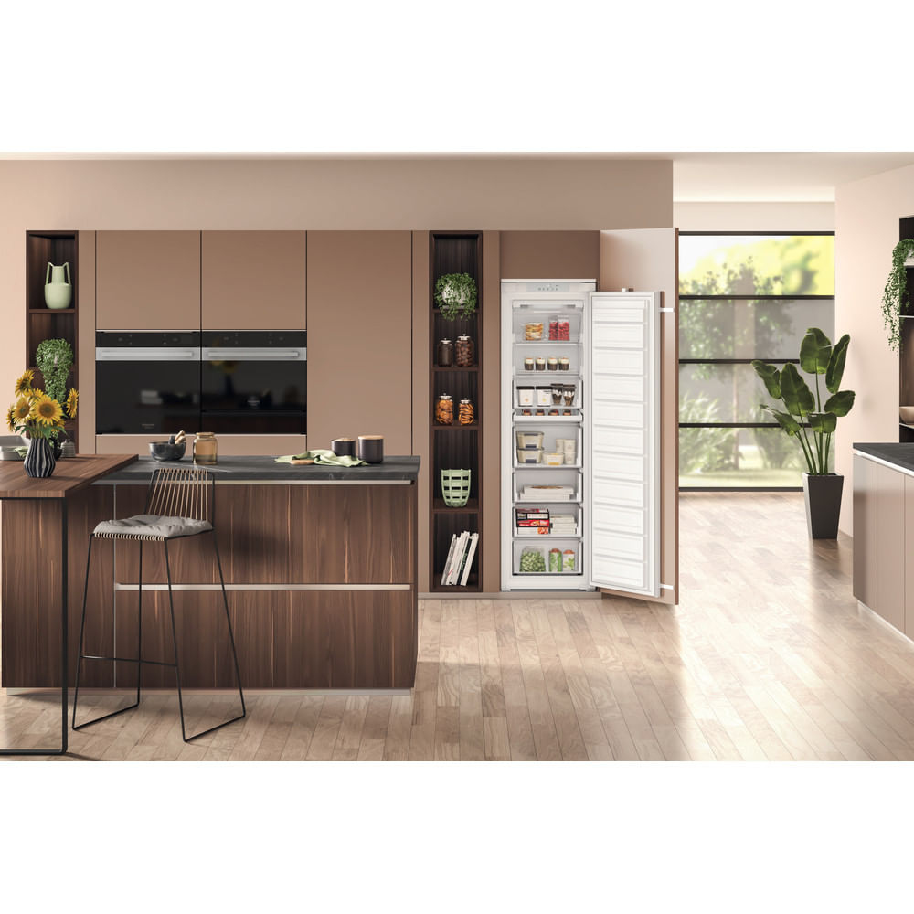 Cucina moderna con congelatore aperto, isola, sgabello e grandi finestre.