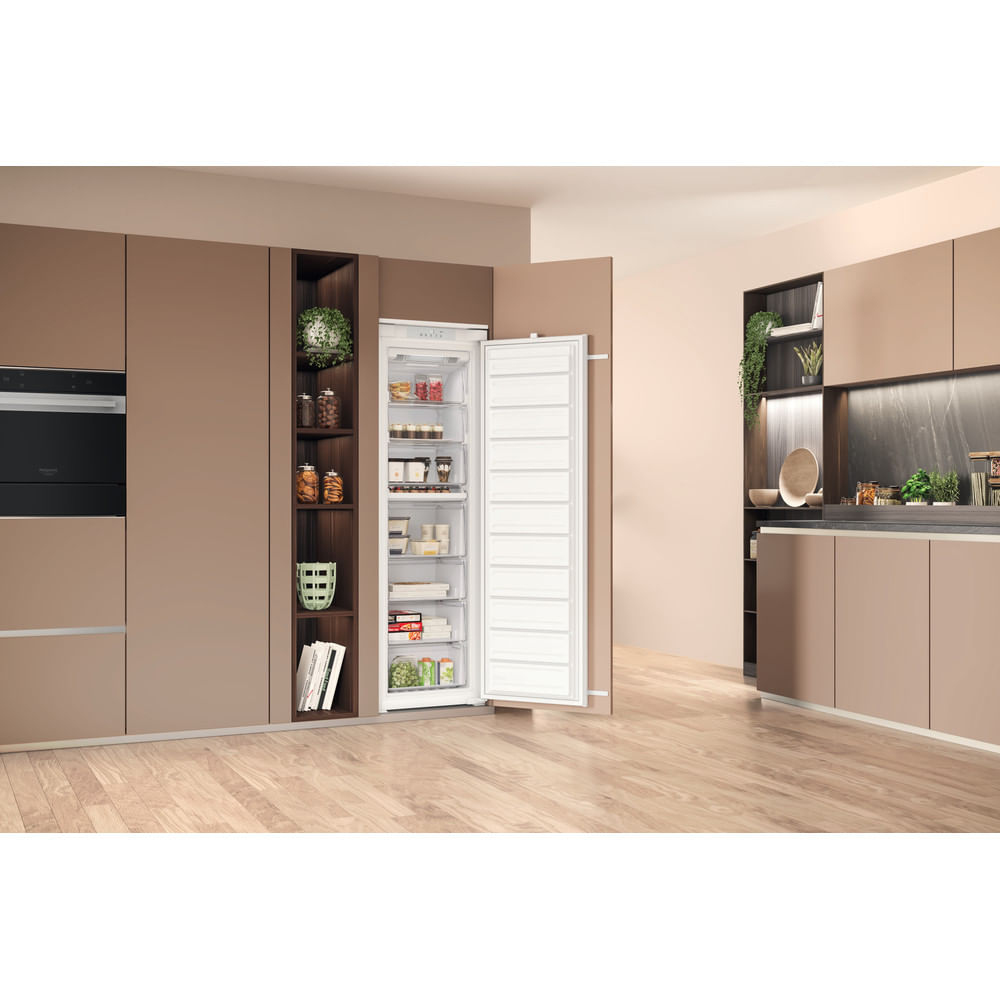 Un congelatore verticale alto con la porta aperta si trova in una cucina moderna con mobili marroni.