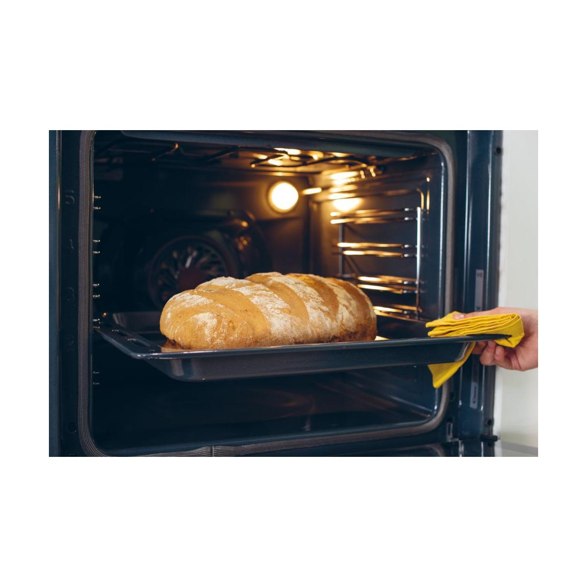 Una pagnotta dorata su una teglia viene rimossa da un forno scuro.