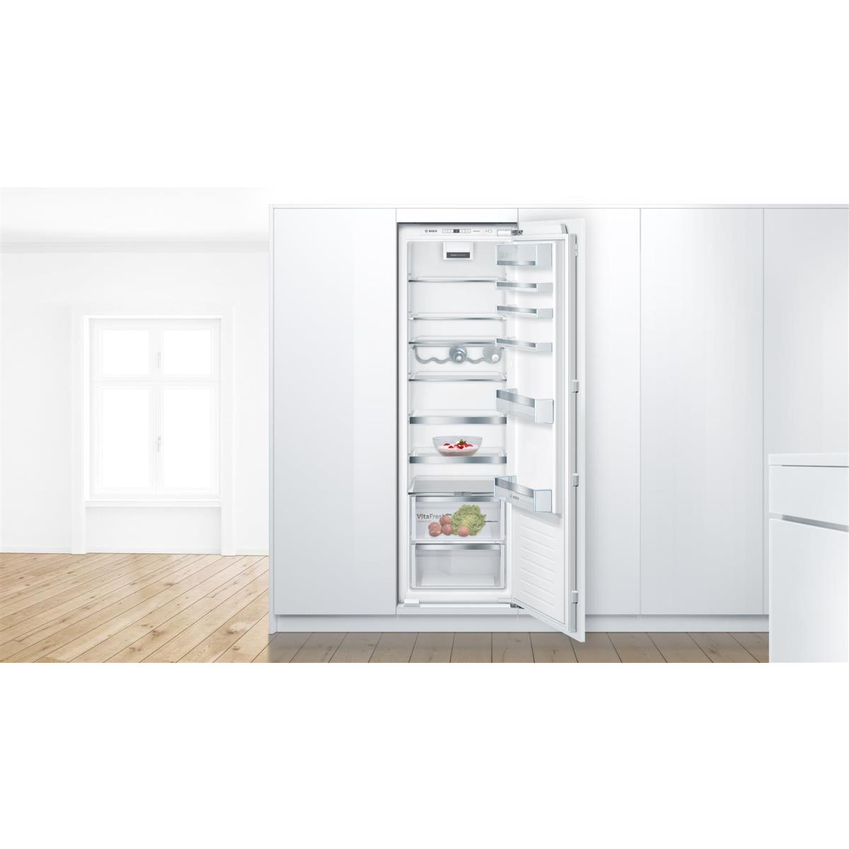 Refrigerador abierto con estantes de cristal y cajones para verduras, junto a una ventana.