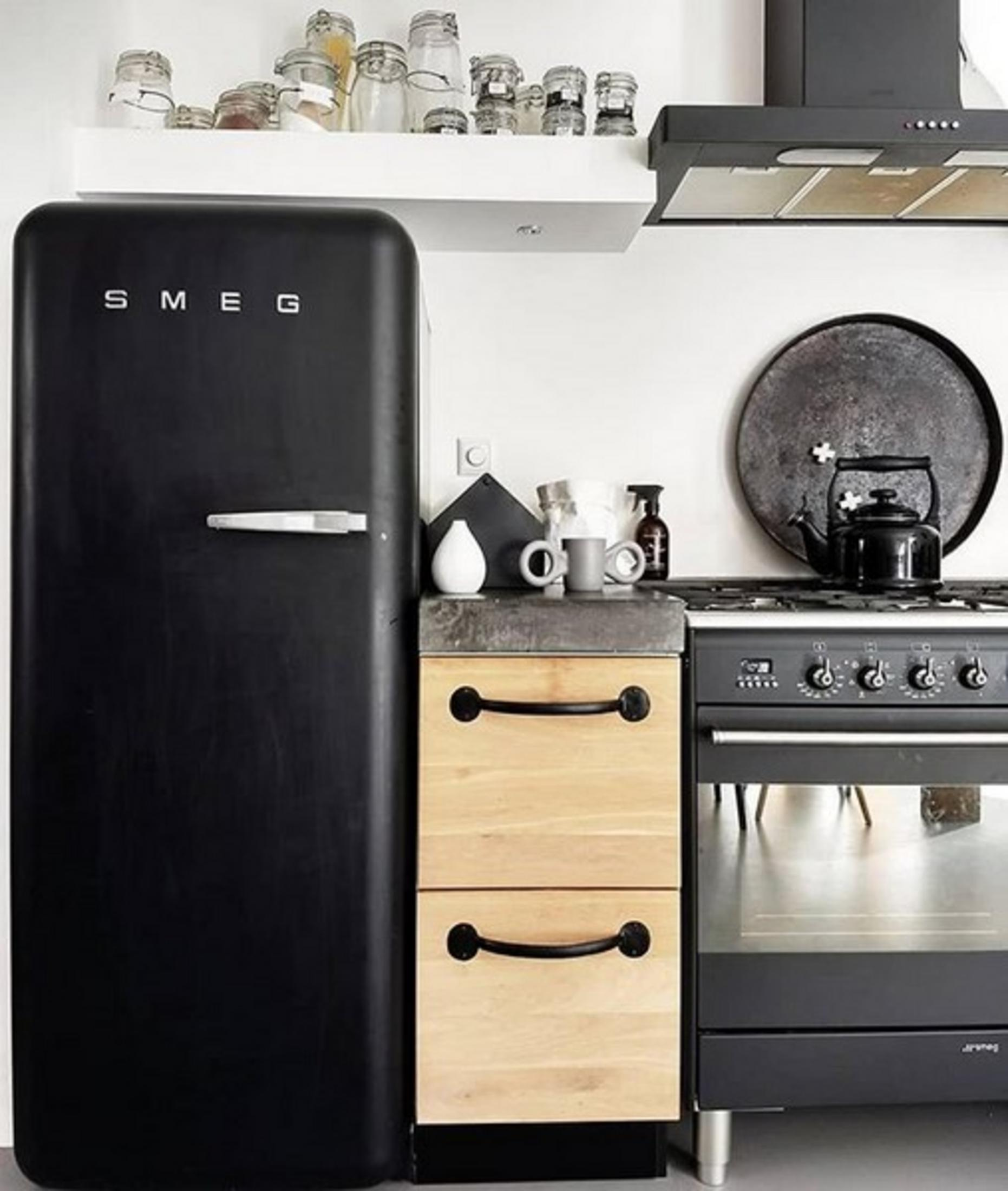 Frigorifero Smeg nero accanto a cassetti in legno e fornelli a gas.