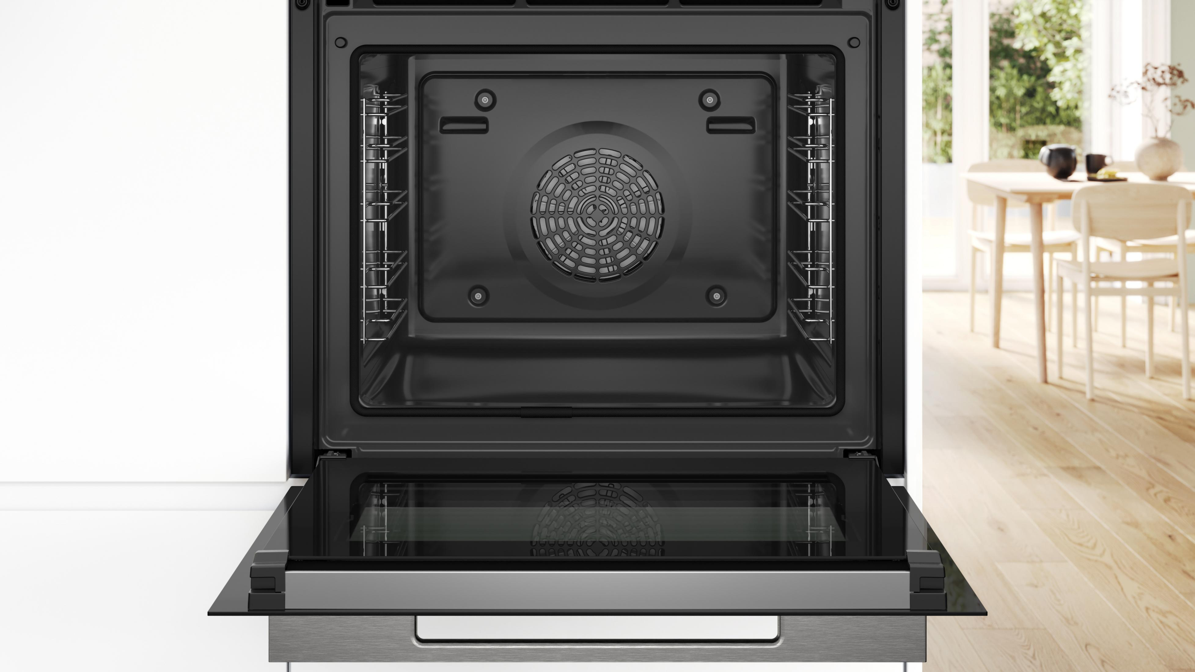 Forno da incasso aperto con griglie argentate e griglia del ventilatore. Fuori un tavolo con sedie.