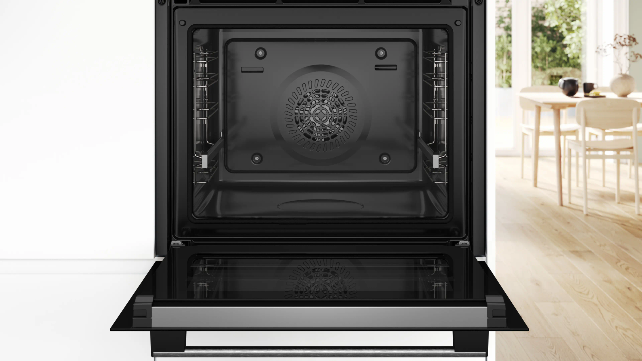 Forno nero aperto con griglie interne, ventola e zona pranzo sfocata sullo sfondo.