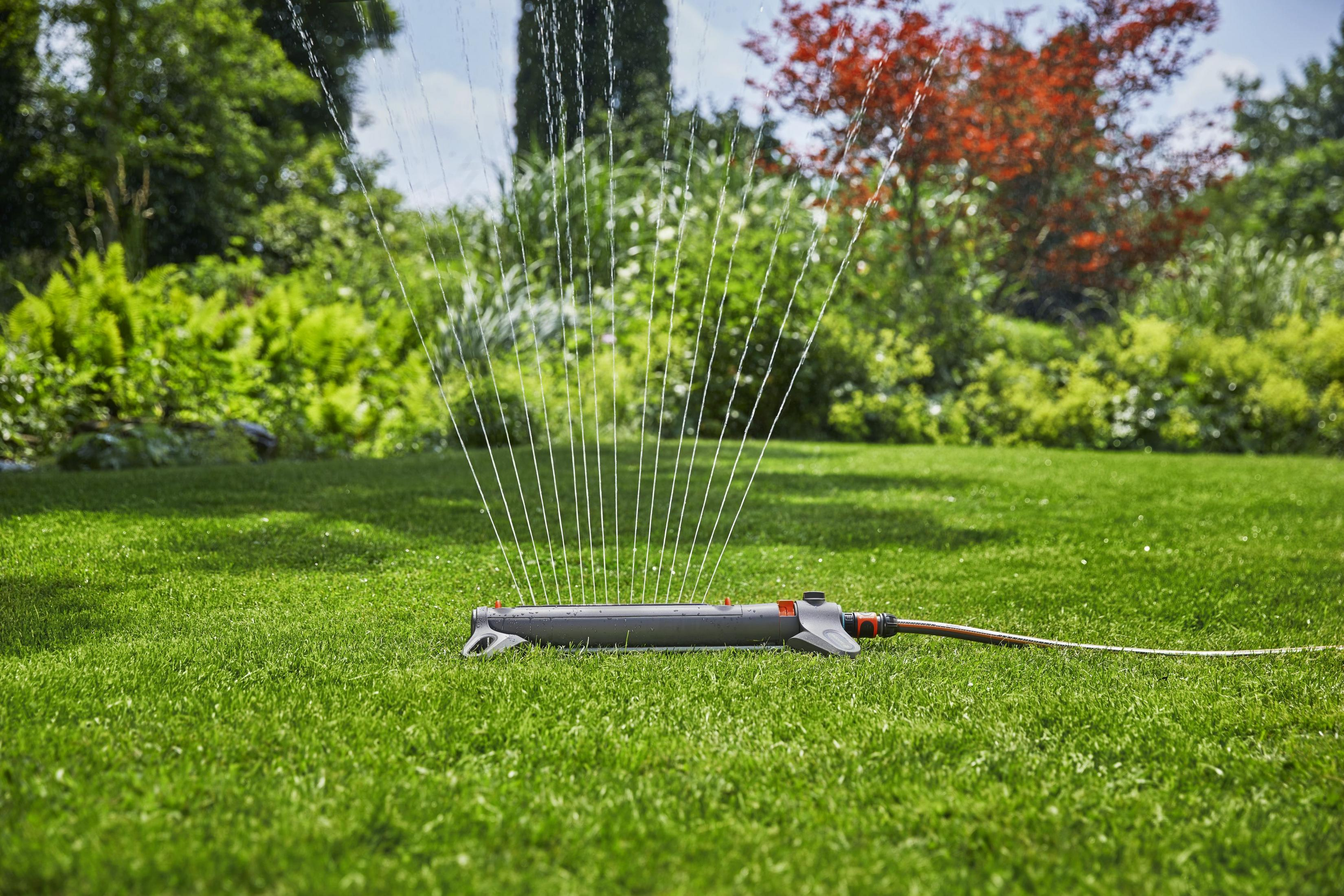 Un irrigatore per prati anna erba verde in un giardino con alberi e cespugli.
