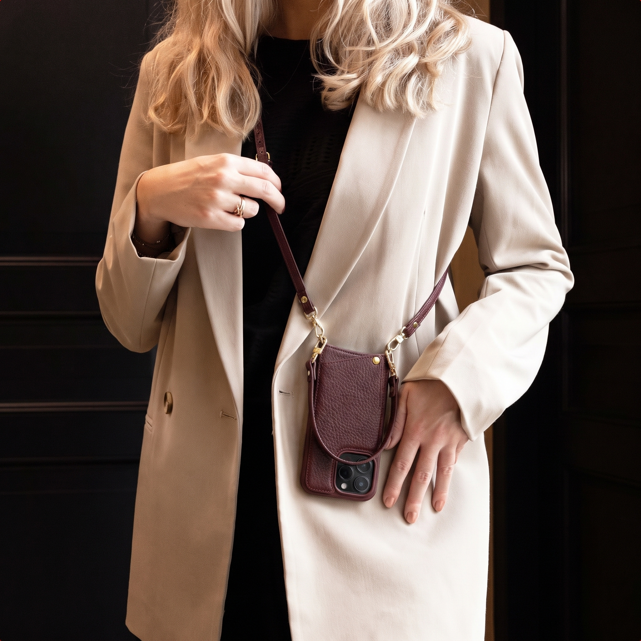 A blonde woman wears a beige blazer and a burgundy phone case on a crossbody strap.