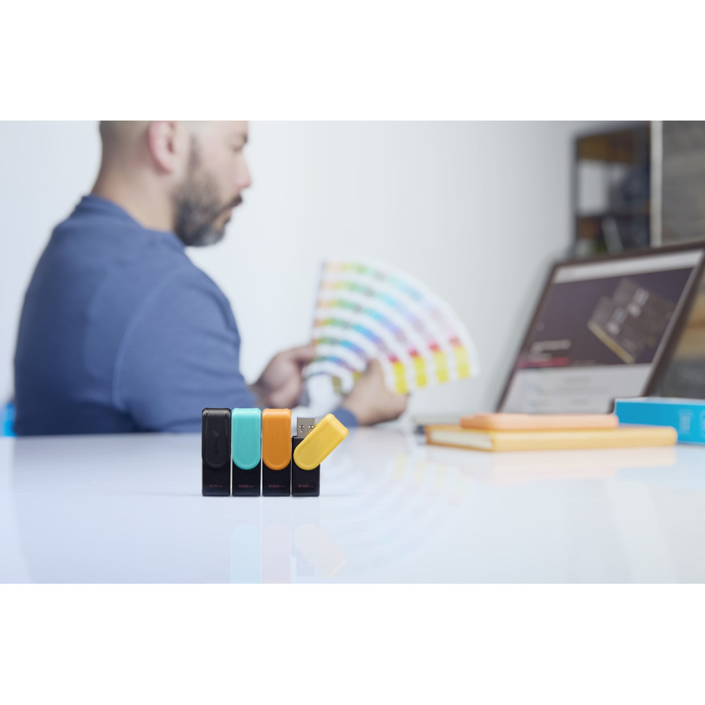 Man with color chart, four USB drives, laptop, and notebook on desk.