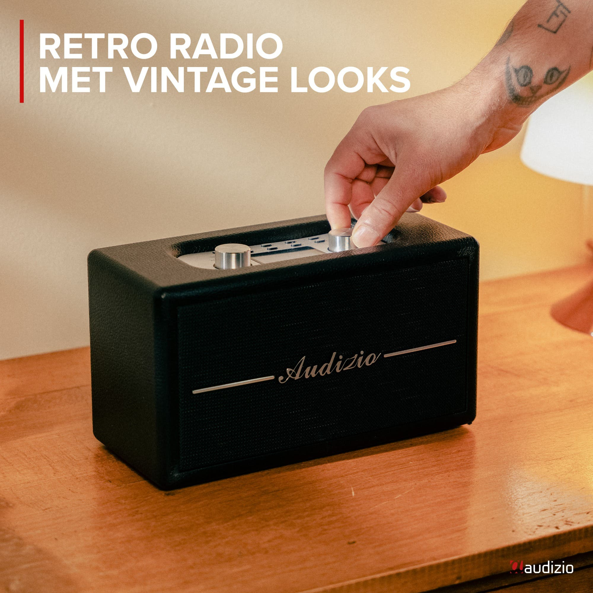 Mano gira perilla en radio retro negra con logo Audizio sobre superficie de madera.