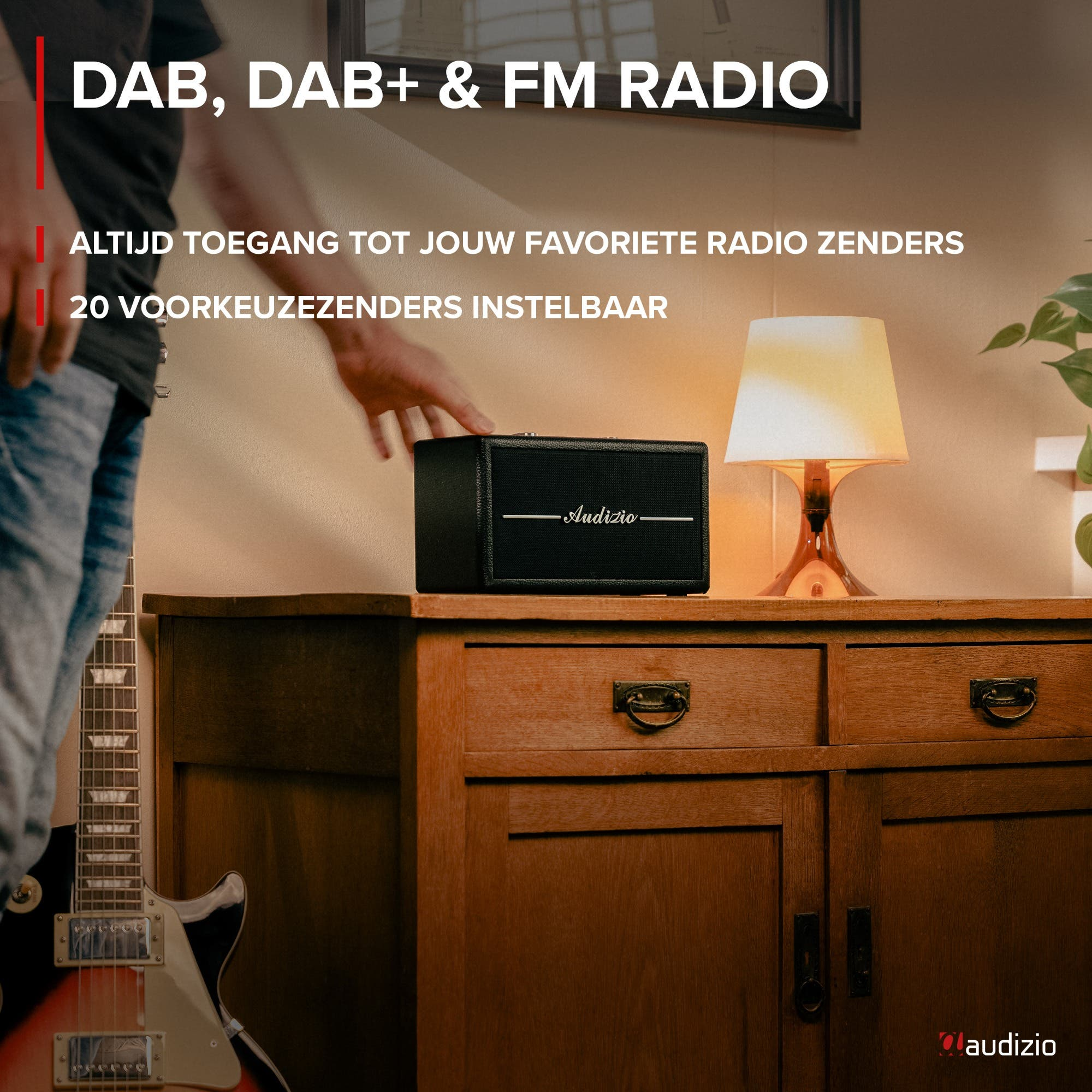 Un hombre toca una radio Audizio negra en un mueble de madera junto a una guitarra.