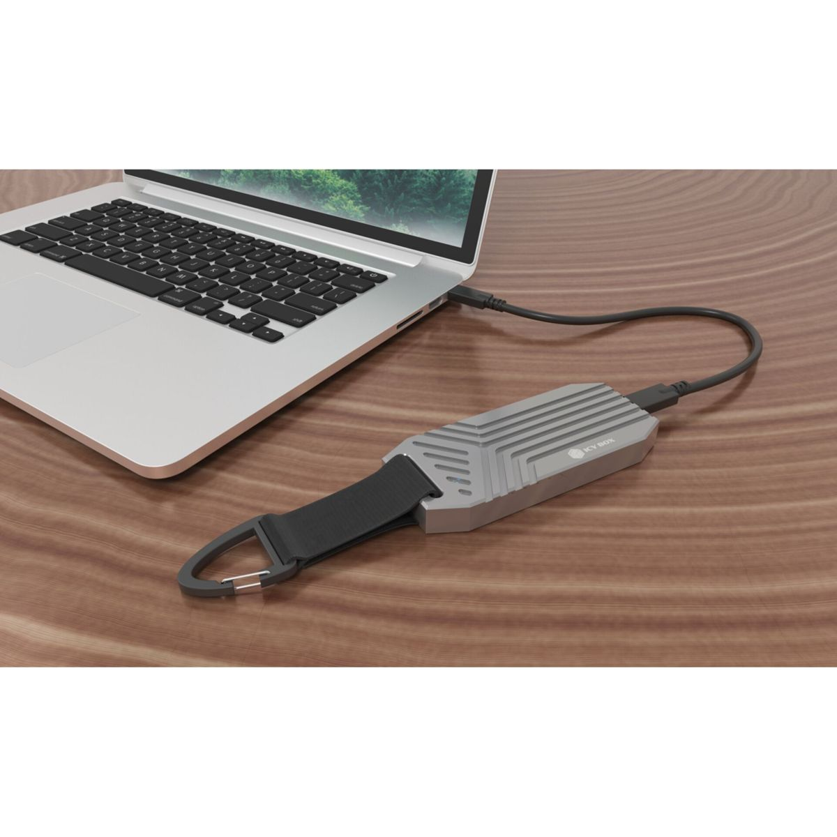 Un disco esterno argentato con cinturino nero è collegato a un laptop su scrivania legno.