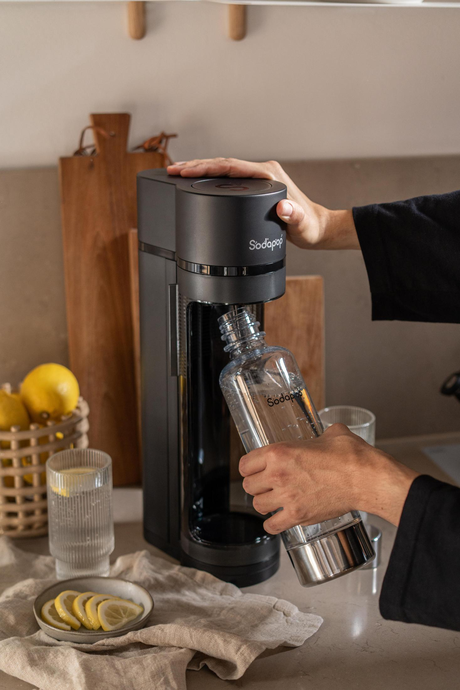 Una mano inserisce una bottiglia SodaStream in una macchina per soda. Fettine di limone nelle vicinanze.