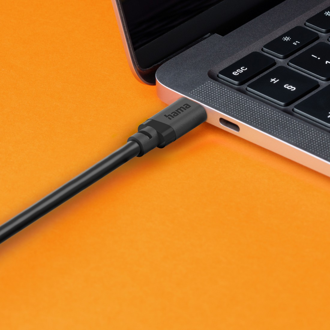 Czarny kabel podłączony do laptopa na pomarańczowym tle.