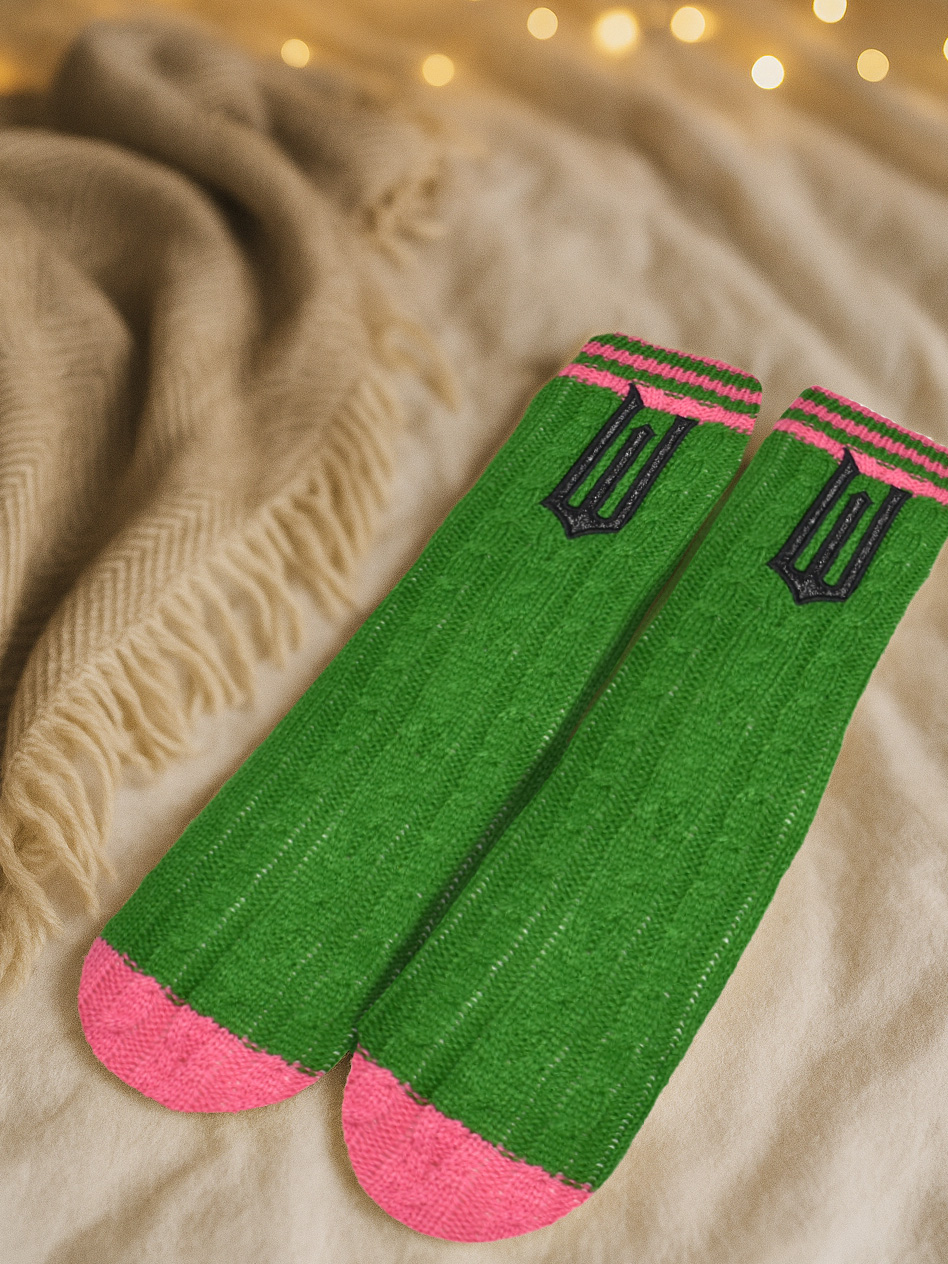 Grüne Stricksocken mit rosa Zehen und gestreiften Bündchen auf einer cremefarbenen Decke.