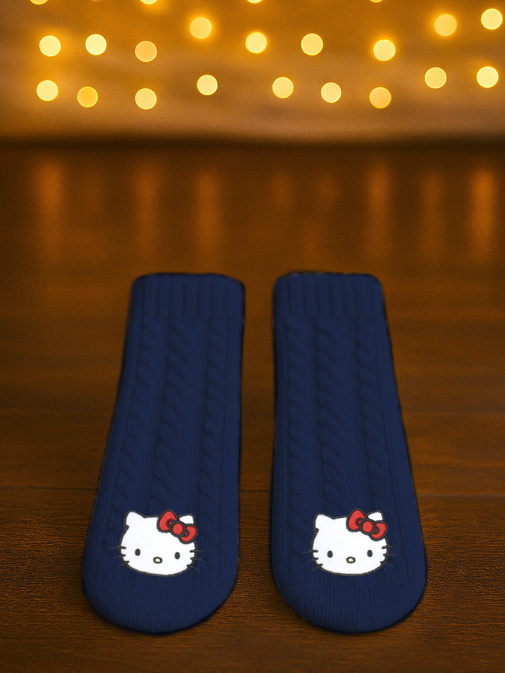Dunkelblaue Socken mit Hello Kitty-Motiv auf Holzboden, Lichter im Hintergrund.