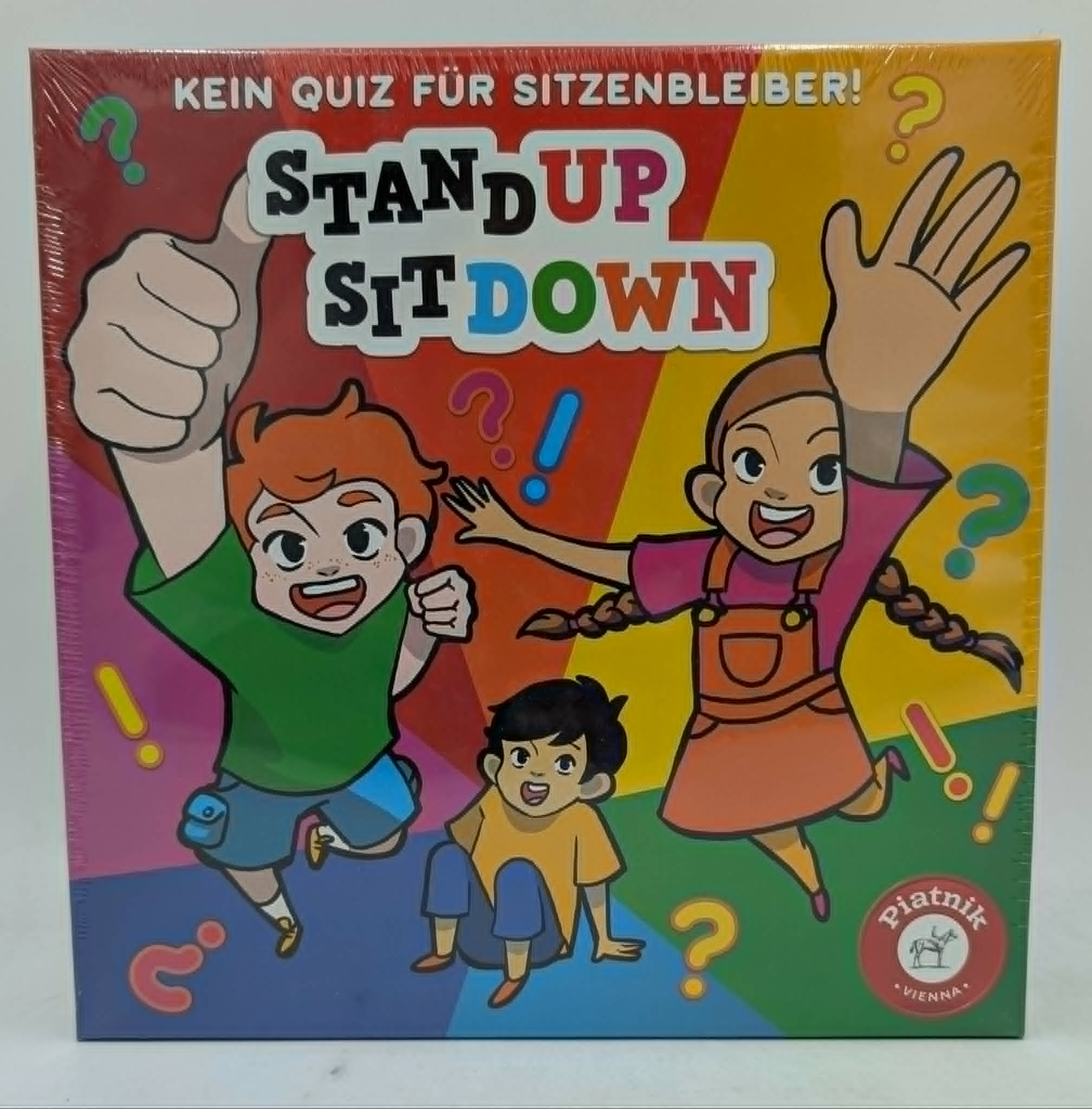 Brettspielcover mit Kindern und Fragezeichen. "Stand Up Sit Down" ist der Titel.