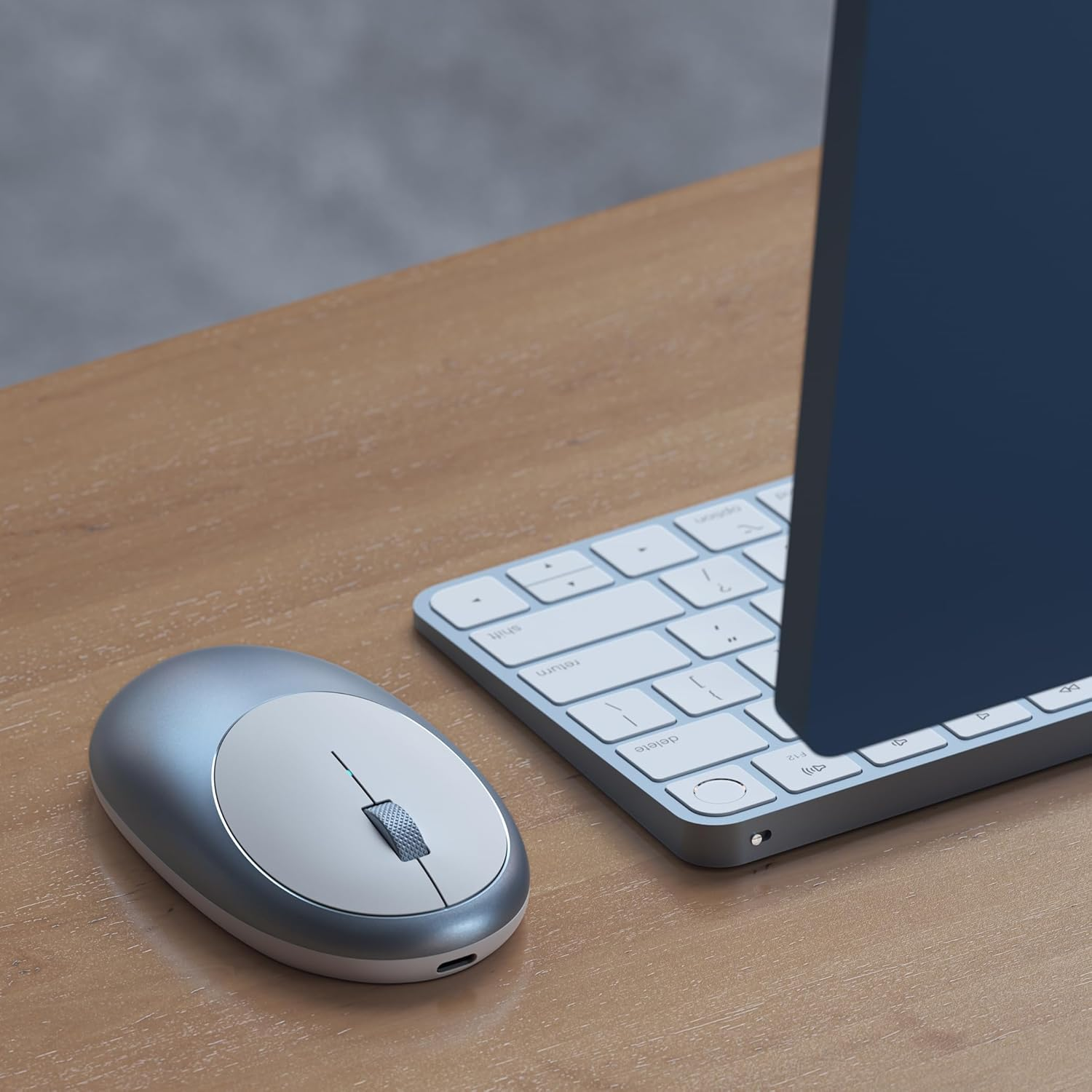 A silver computer mouse and a white keyboard sit on a wooden desk.