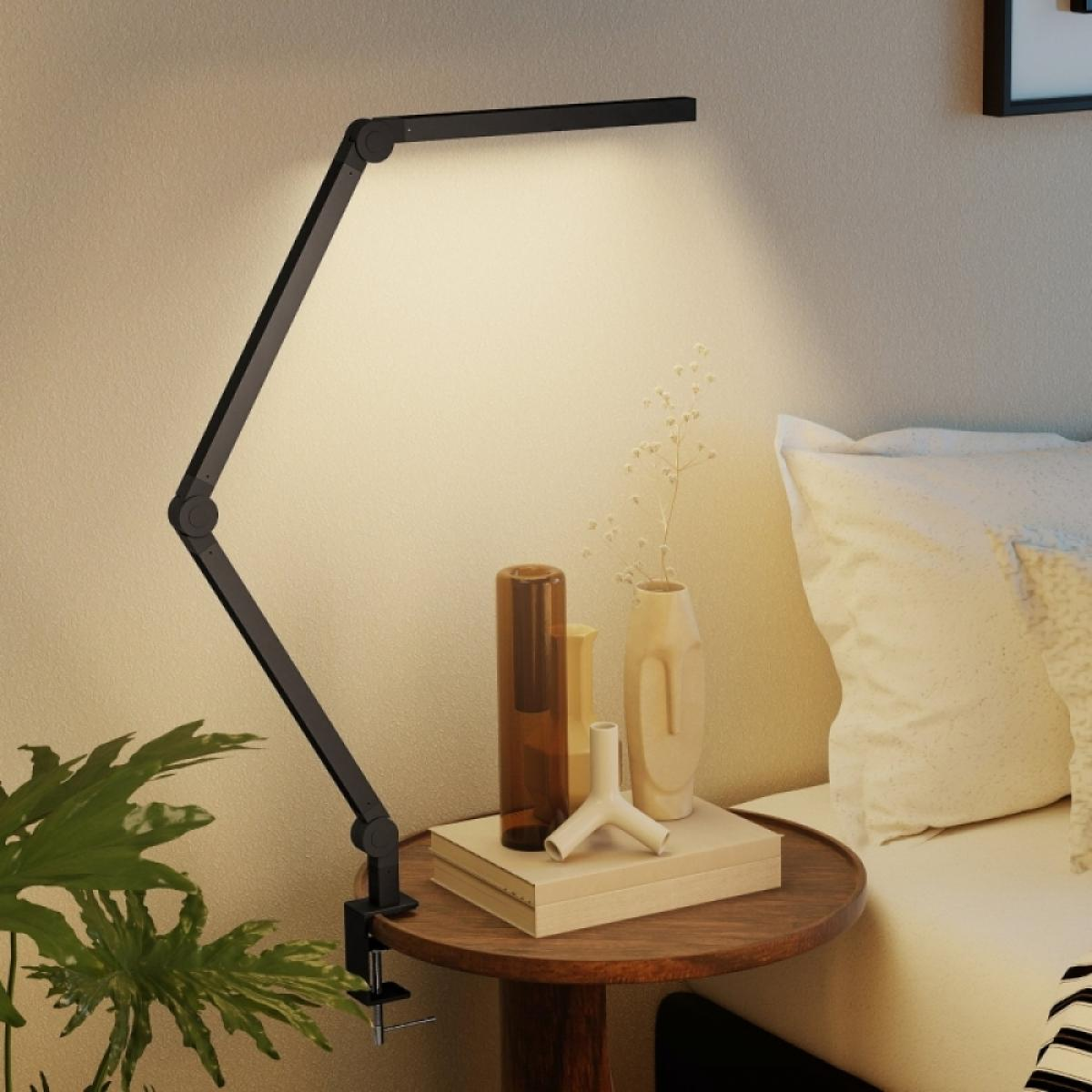 Ein schwarzer Gelenkarm-Schreibtisch mit LED-Licht beleuchtet einen Nachttisch mit Vasen und Büchern.