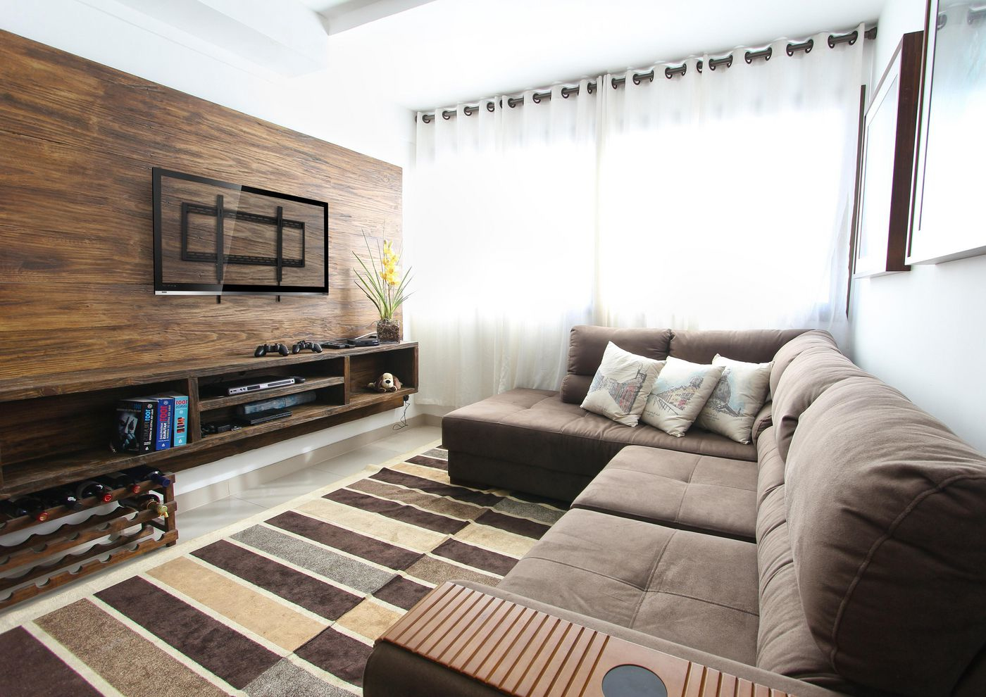 Ein Wohnzimmer mit brauner Couch, Holzwand, Fernseher und gestreiftem Teppich.