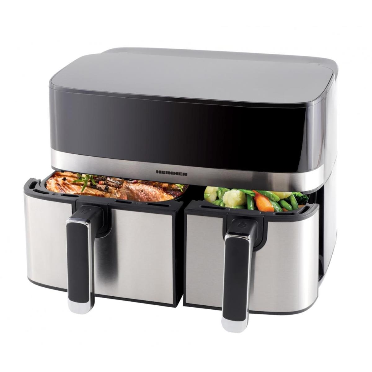 Een zilverkleurige en zwarte Heinner airfryer met twee manden, gevuld met vlees en groenten.