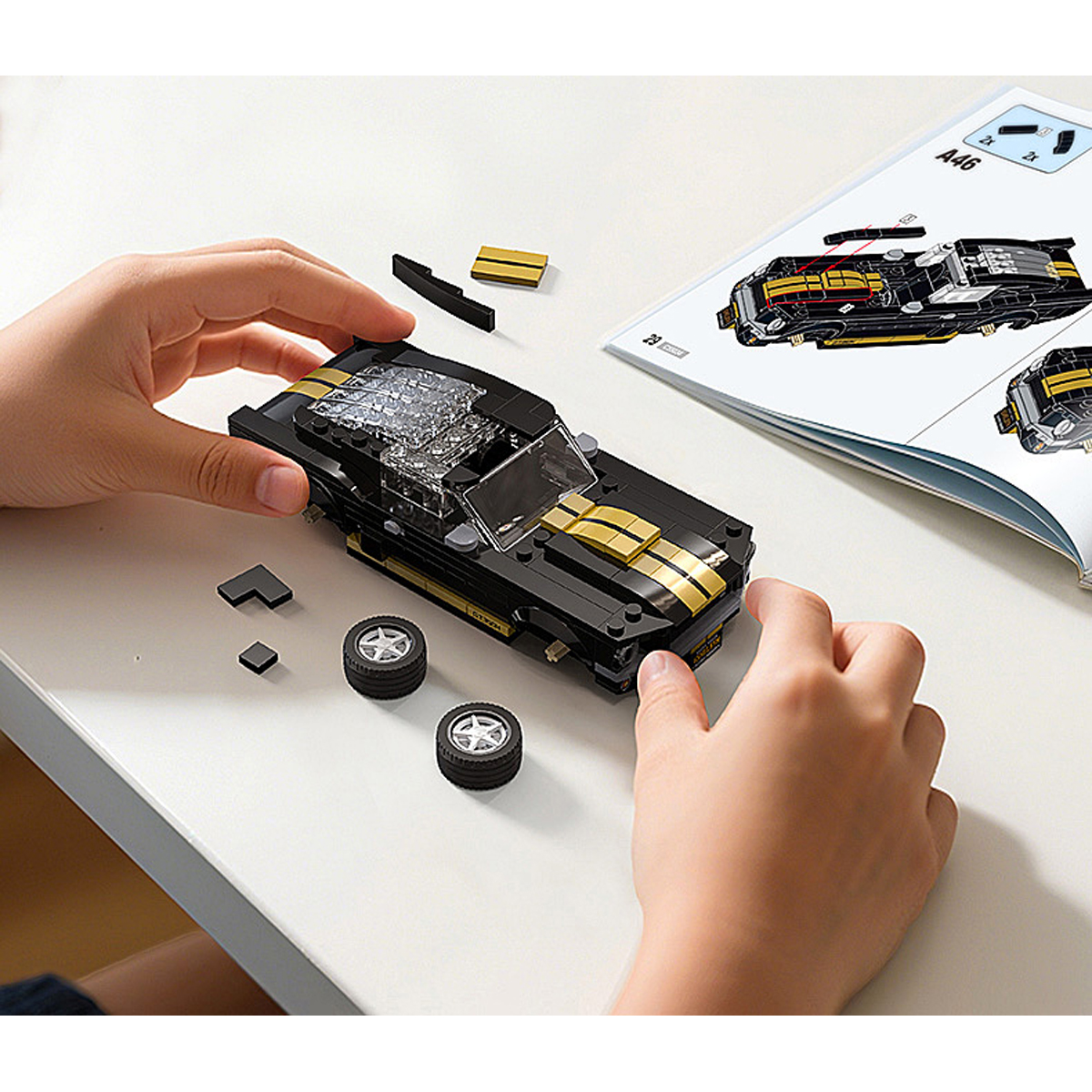 Schwarz-goldenes Lego-Auto auf weißem Tisch, Hände bauen es neben Anleitung.