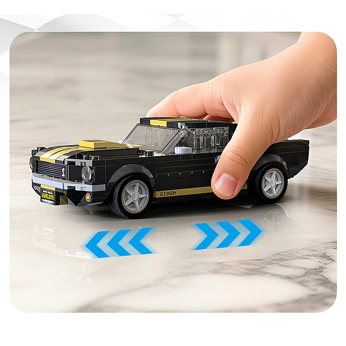 Ein Kind hält einen schwarzen Lego-Sportwagen mit gelben Streifen. Blaue Pfeile deuten Bewegung an.