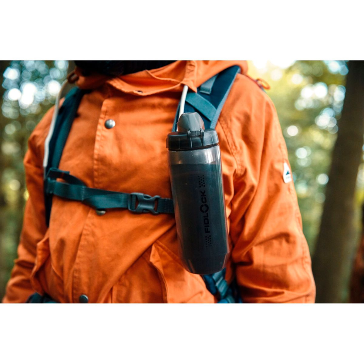 Eine Person in einem orangefarbenen Rucksack mit einer schwarzen Wasserflasche, die daran befestigt ist.