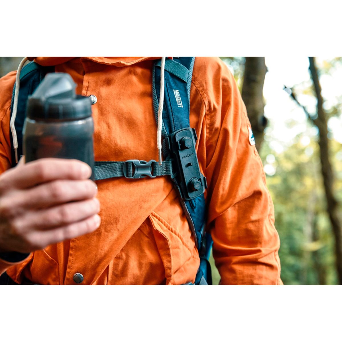 Mann in orangefarbener Jacke hält Wasserflasche, Rucksack mit Halterung.